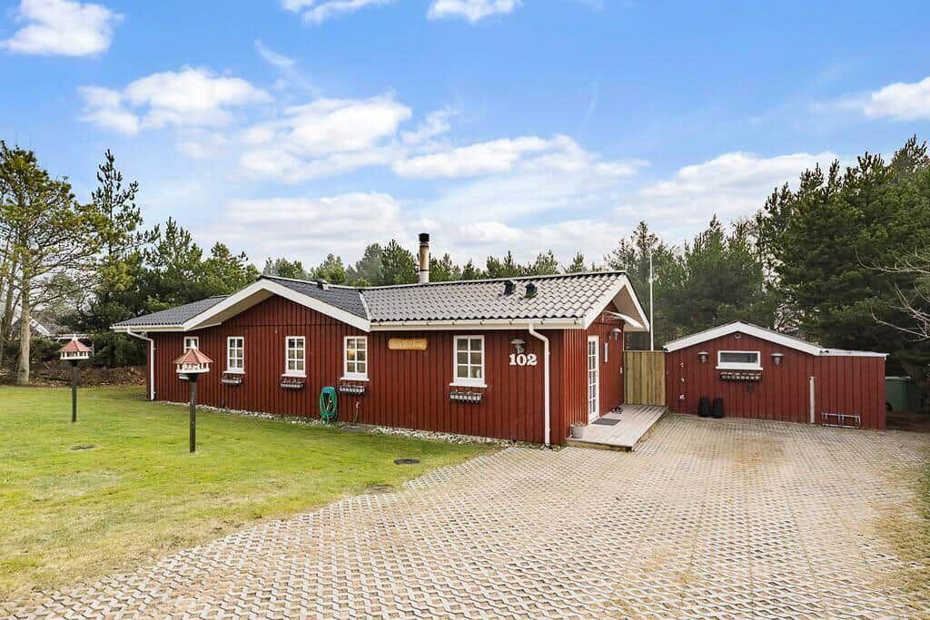 Rotes Holzhaus mit Garage und gepflastertem Hof im Wald.