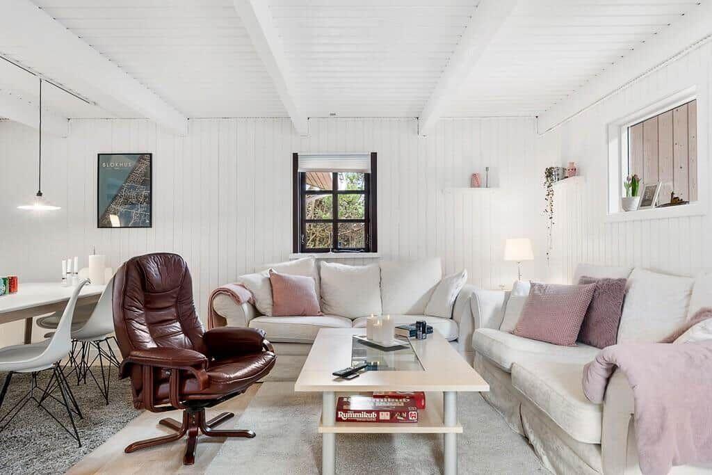 Wohnzimmer mit weißen Wänden, Sofa, braunem Sessel und Tisch.