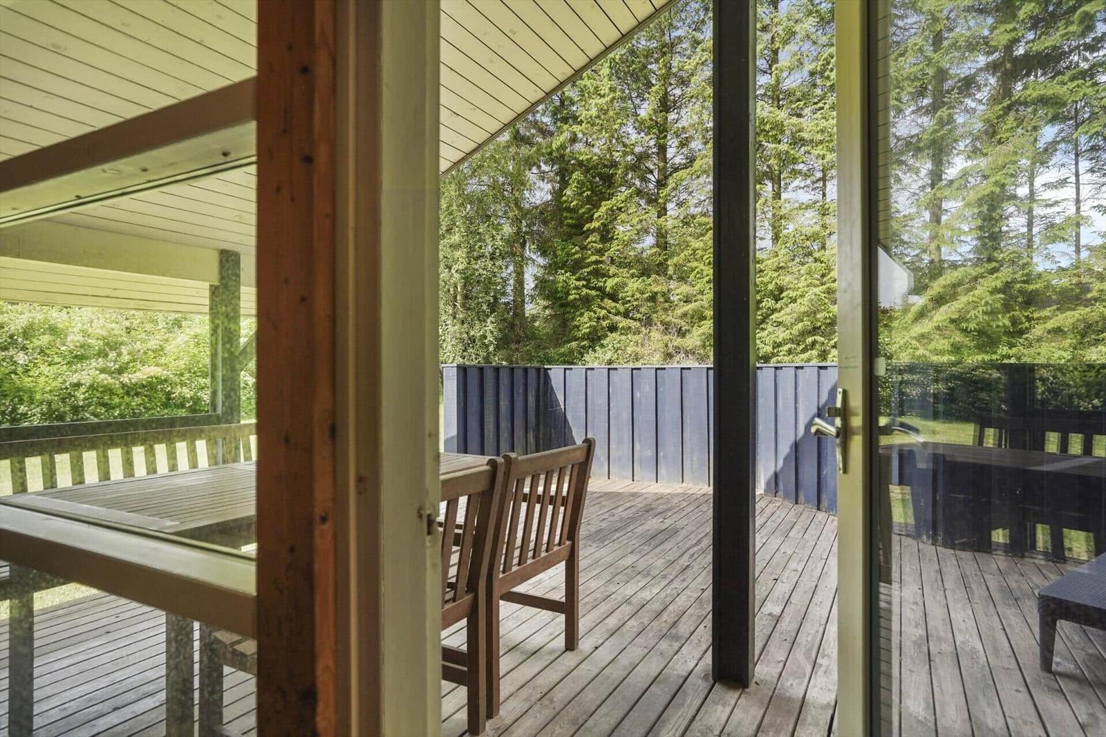 Terrasse mit Holztisch und Stühlen, umgeben von Wald und blauem Zaun.