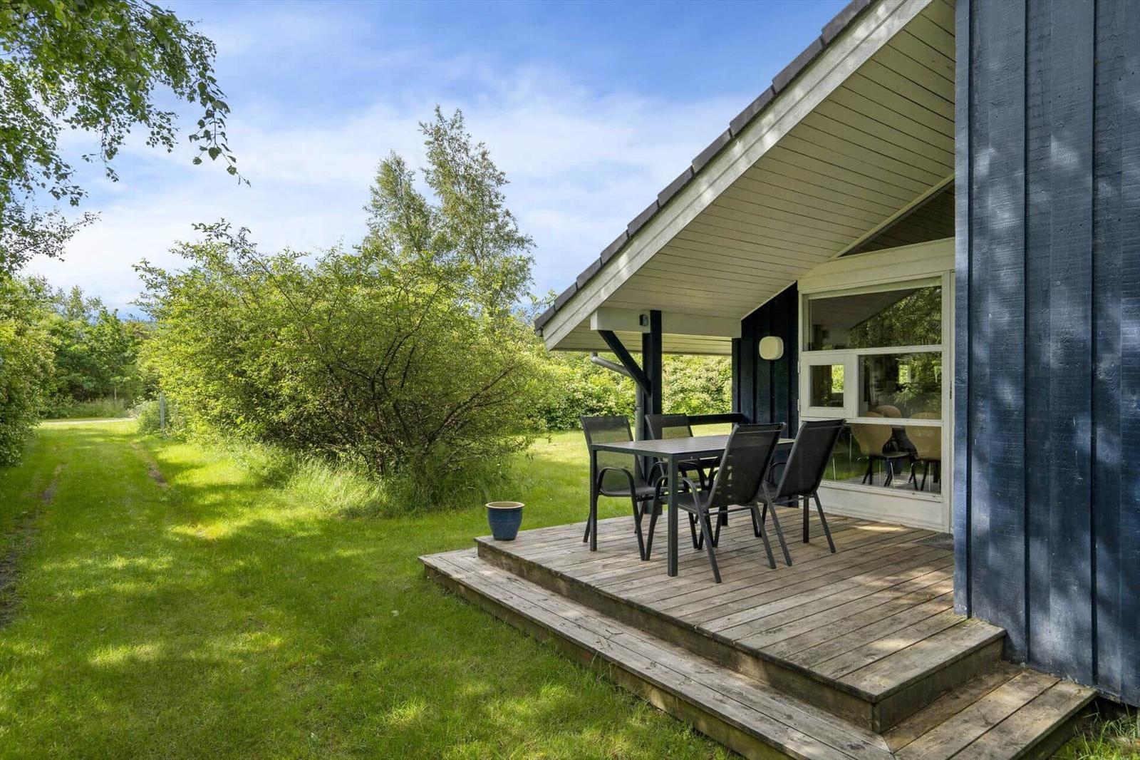 Terrasse mit Tisch und Stühlen vor einem Haus mit Holzveranda und grünem Garten.