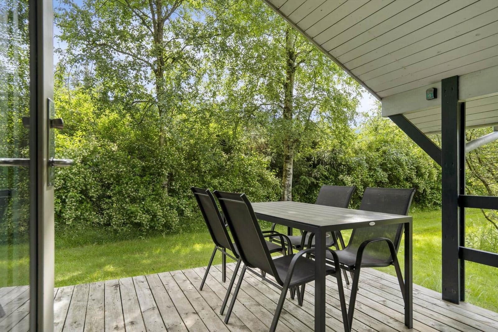 Terrasse mit Tisch und Stühlen, umgeben von grüner Vegetation und einem Holzdeck.