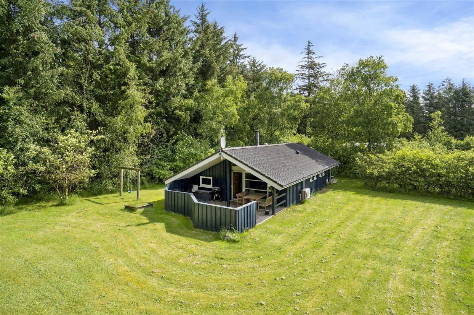 Hütte mit Terrasse, Grill und Schaukel im grünen Garten.