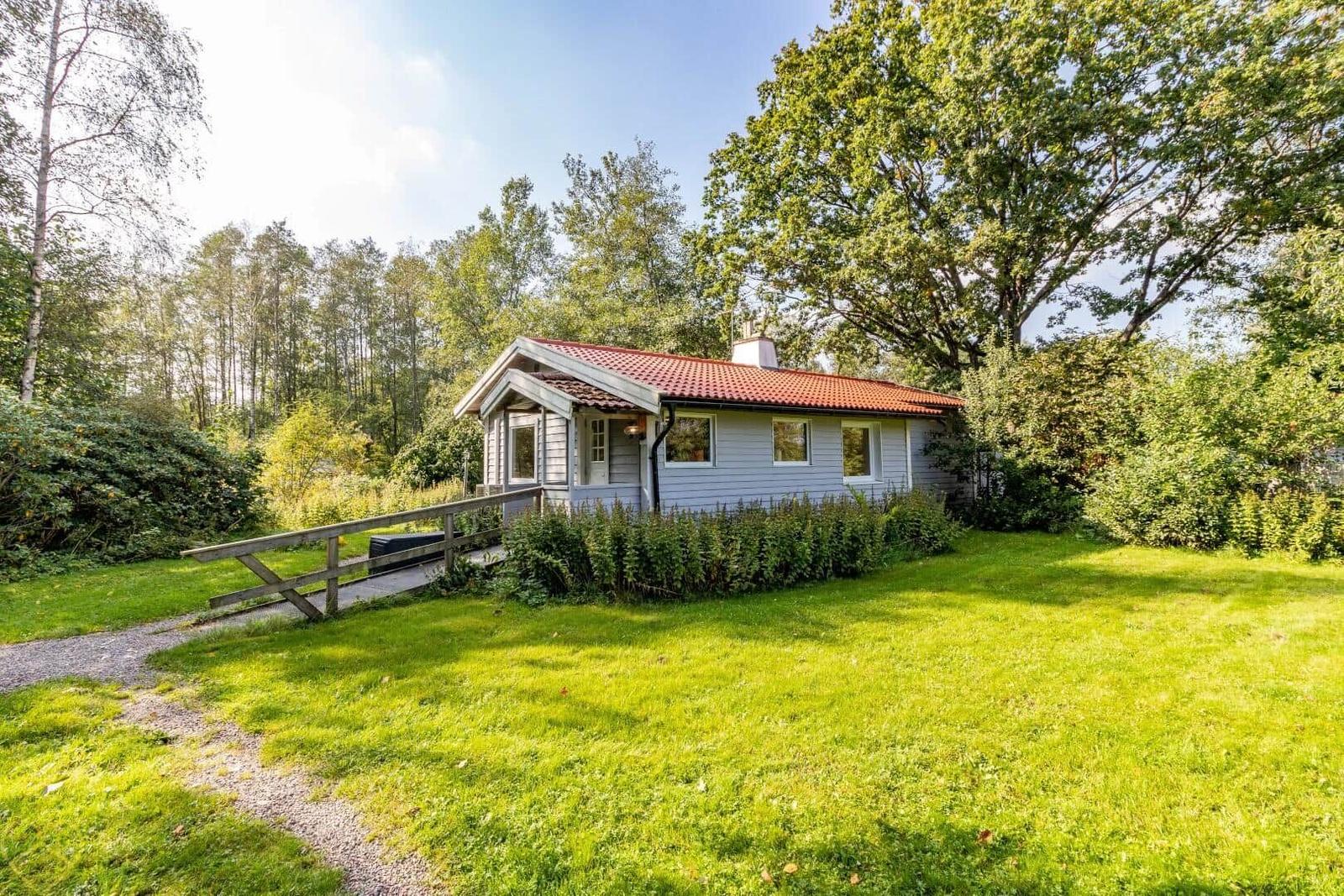Ein kleines Haus mit rotem Dach steht auf einer grünen Wiese umgeben von Bäumen.