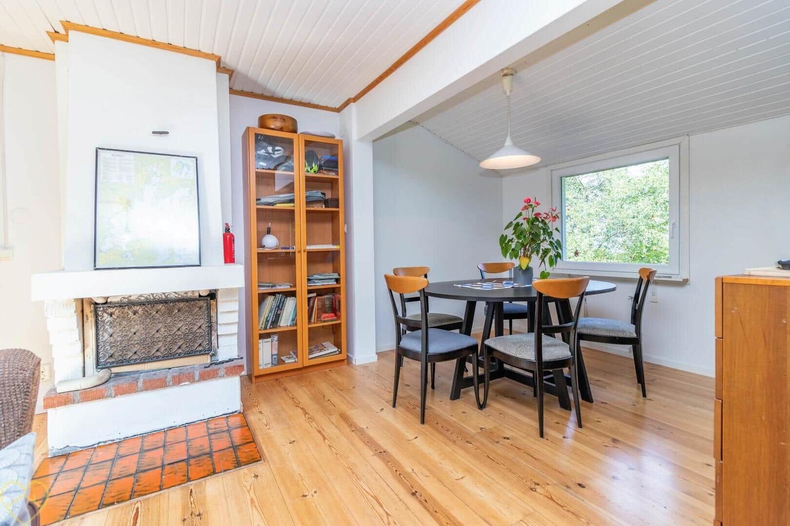 Essbereich mit Tisch, Stühlen und Fenster. Kamin und Bücherregal im Hintergrund.