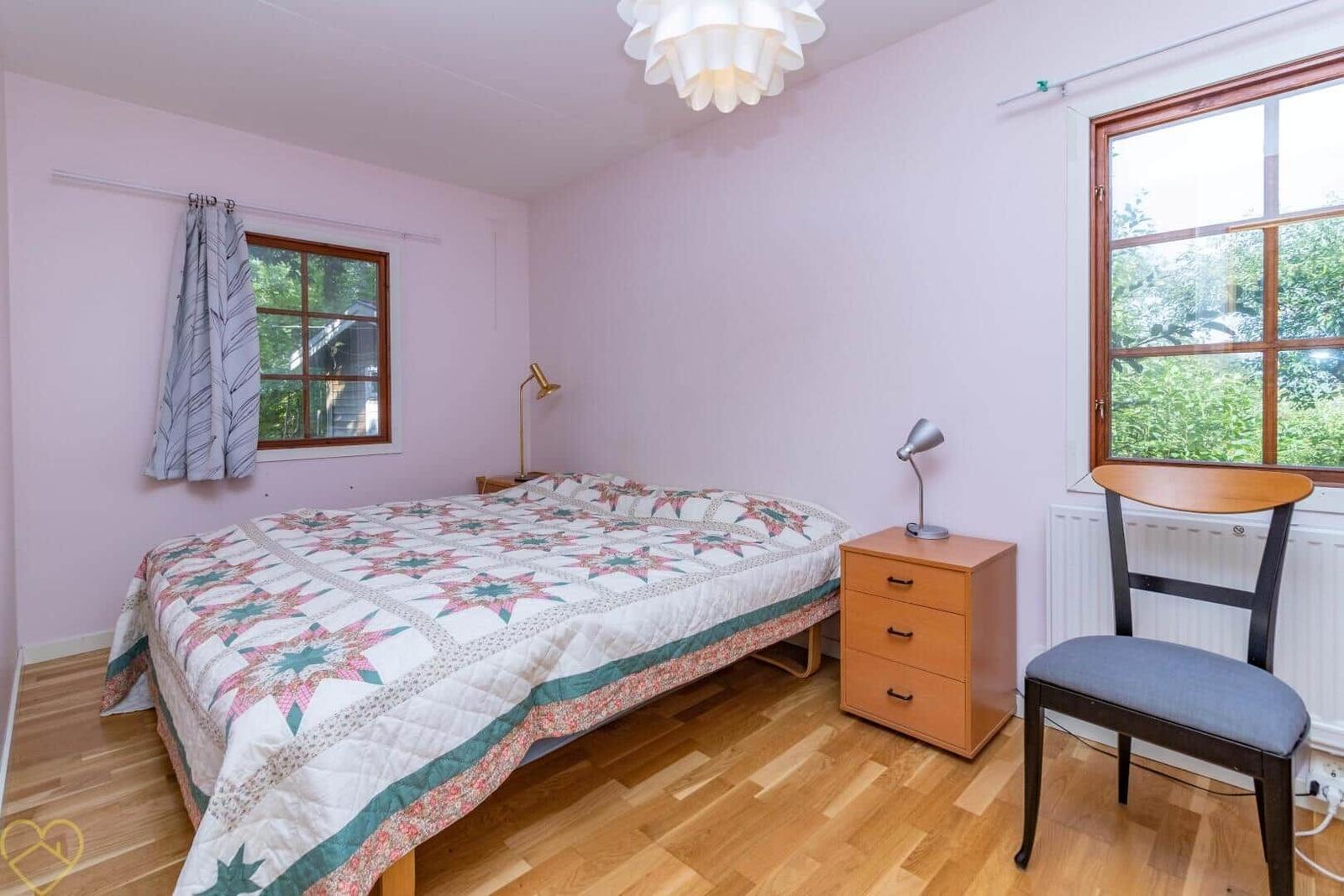 Schlafzimmer mit Bett, Nachttisch und Stuhl. Fenster mit Blick auf Grün.