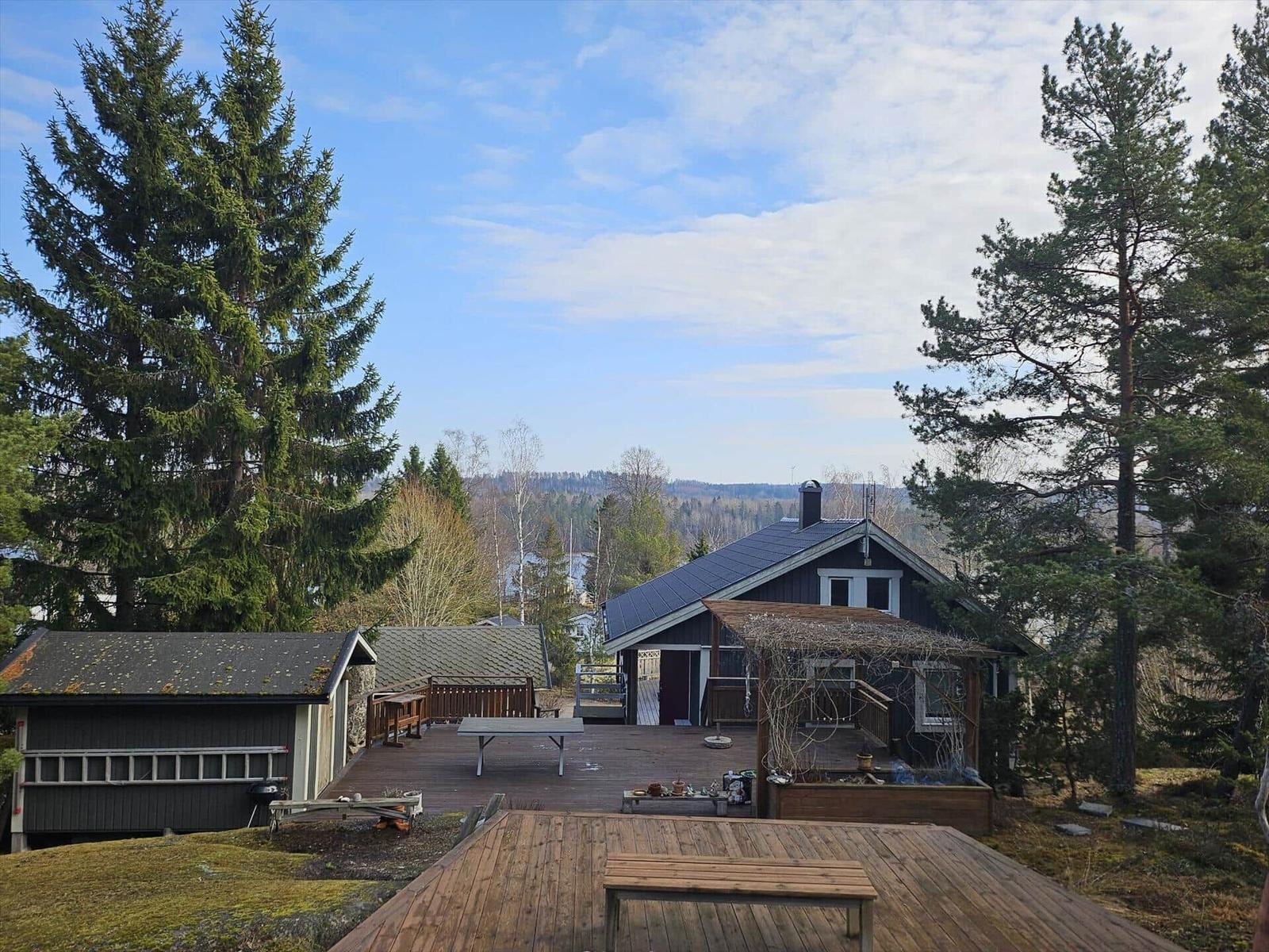 Haus mit Holzterrasse, Grillplatz und Blick auf Wald und Berge.