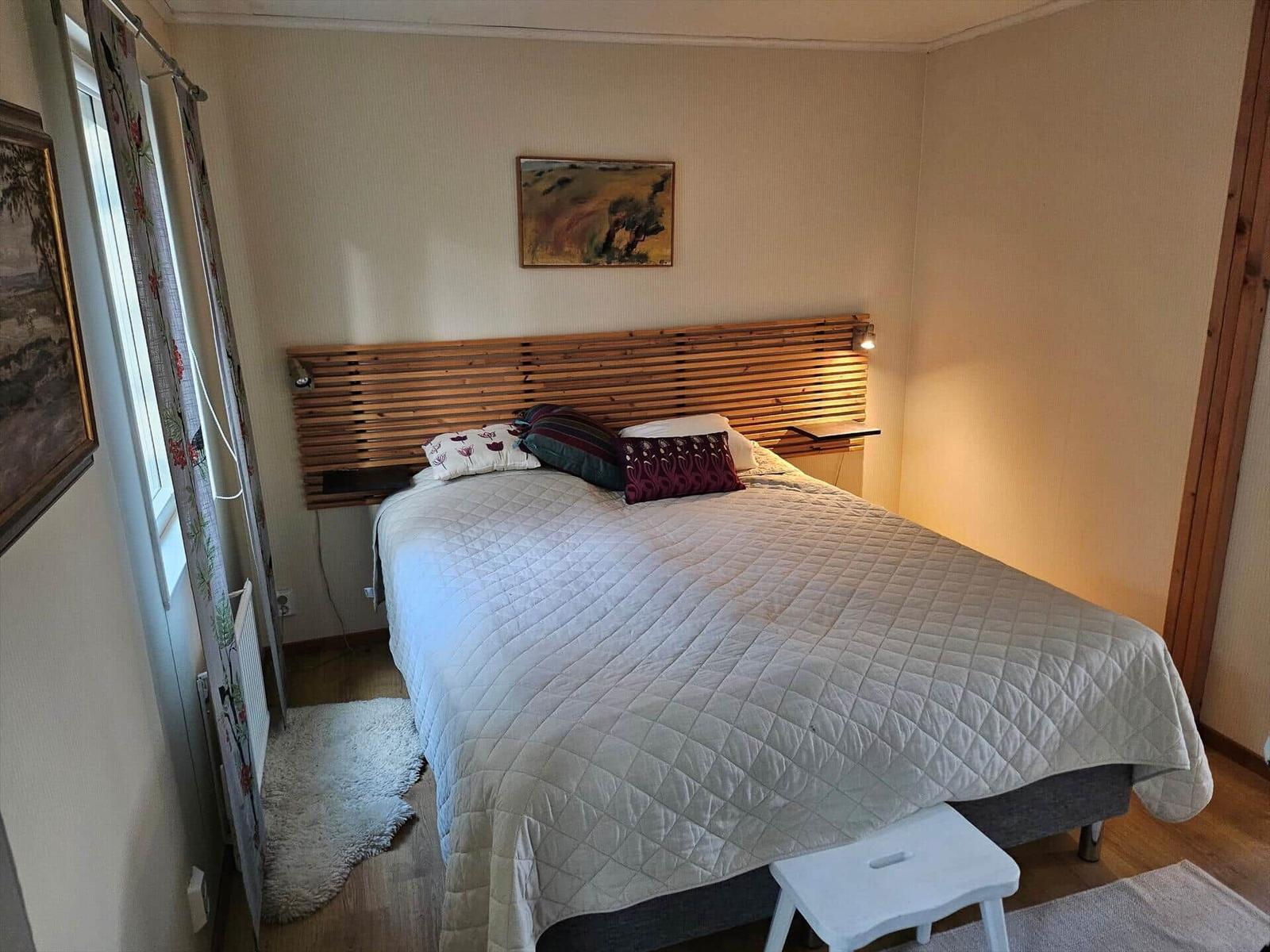 Schlafzimmer mit Bett, Holzkopfteil und Wandbild.