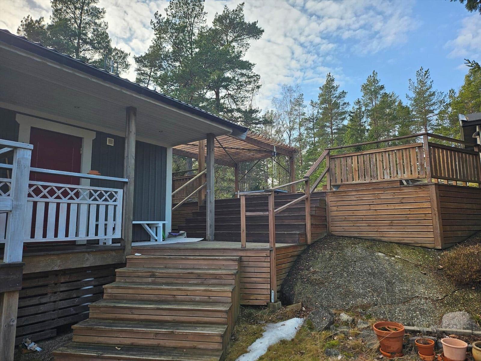 Holzterrasse mit Stufen und Balkon vor einem Haus in Waldnähe.