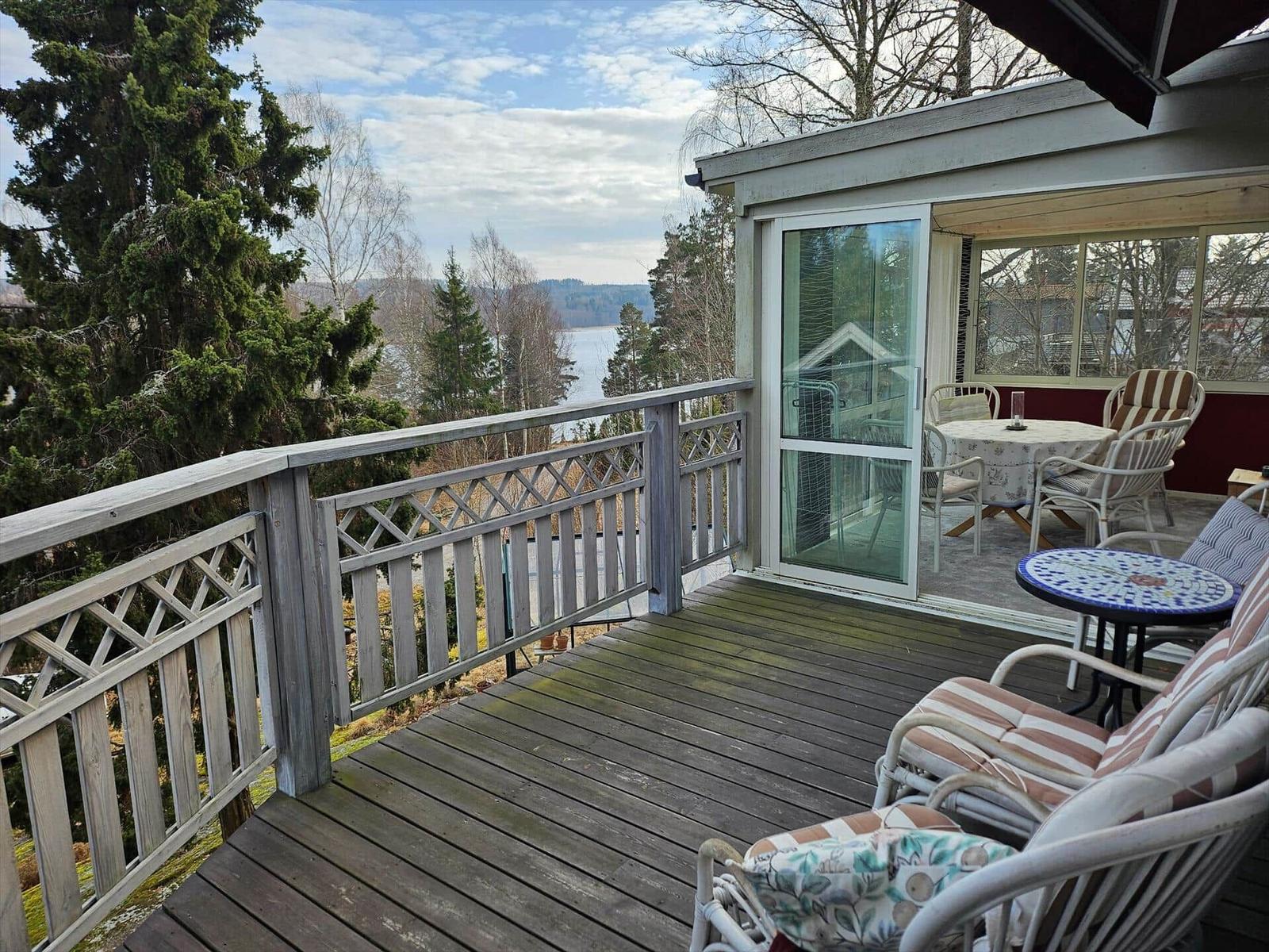 Terrasse mit Blick auf See und Bäume, mit Sitzgelegenheiten und Schiebetür.