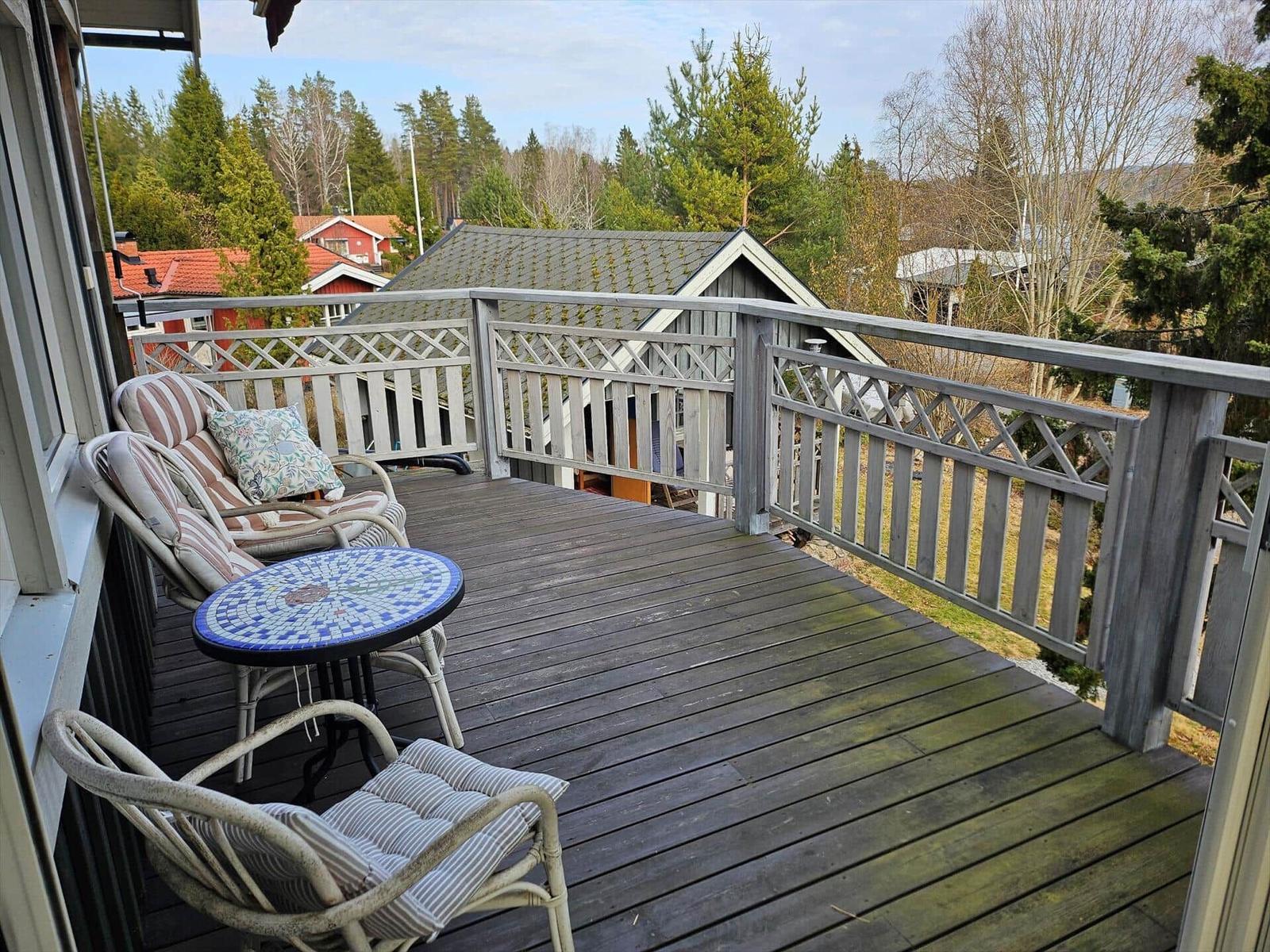 Terrasse mit Holzboden, Gartenmöbel und Blick auf Wald und Häuser.