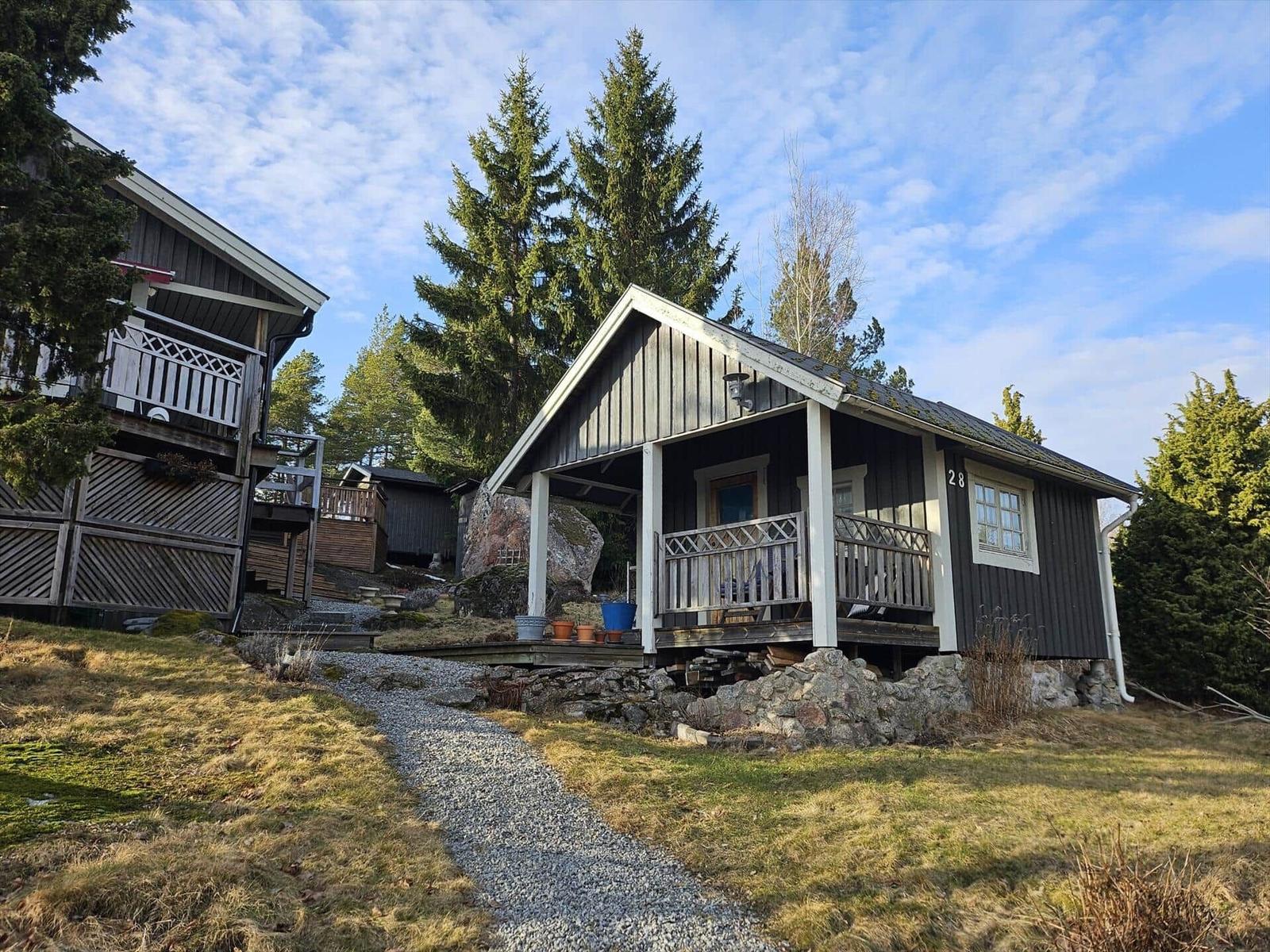 Holzhütte mit Veranda, umgeben von Bäumen und Steinweg.