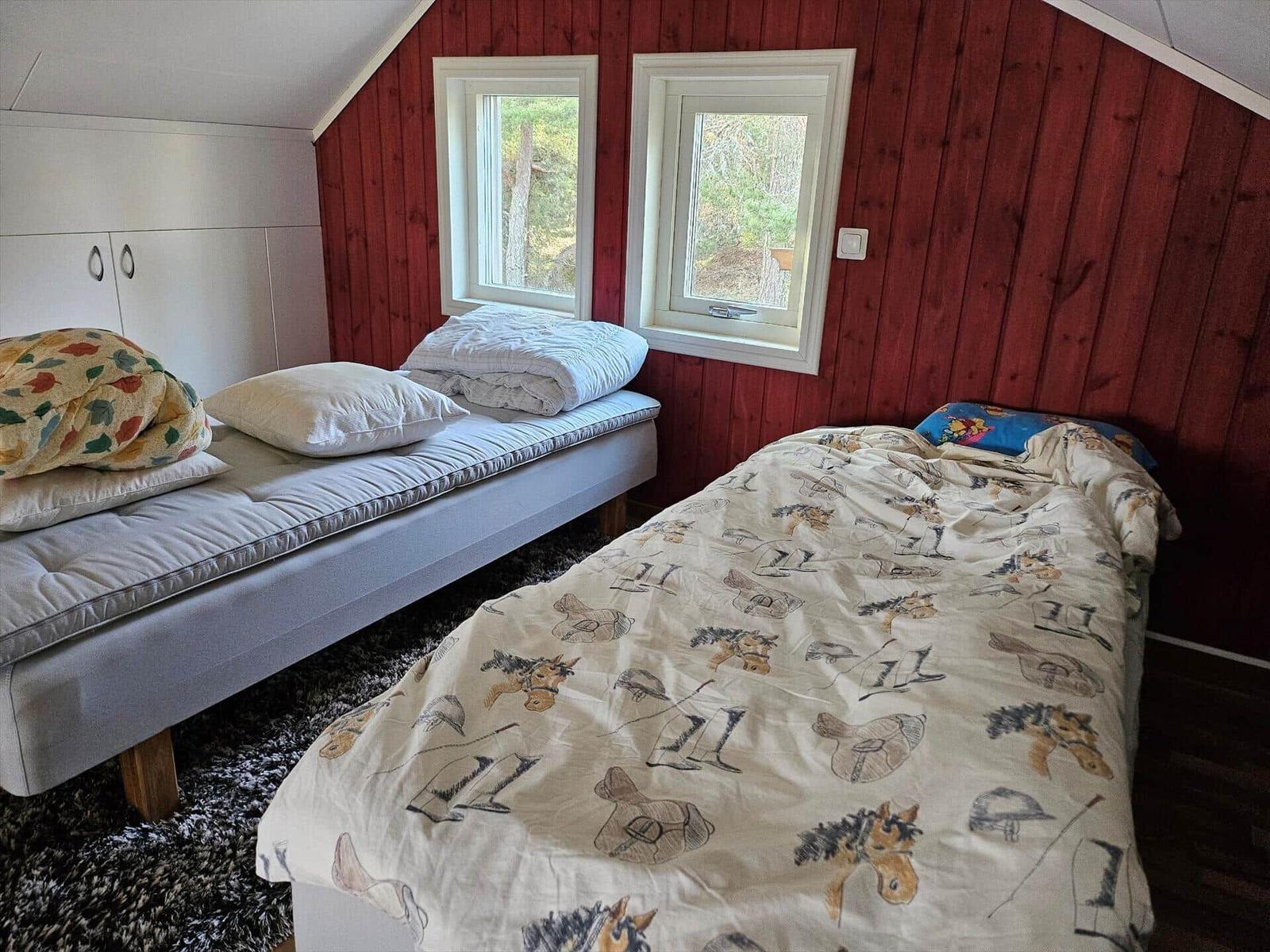 Zimmer mit zwei Betten, roten Wänden und zwei Fenstern mit Blick auf Wald.