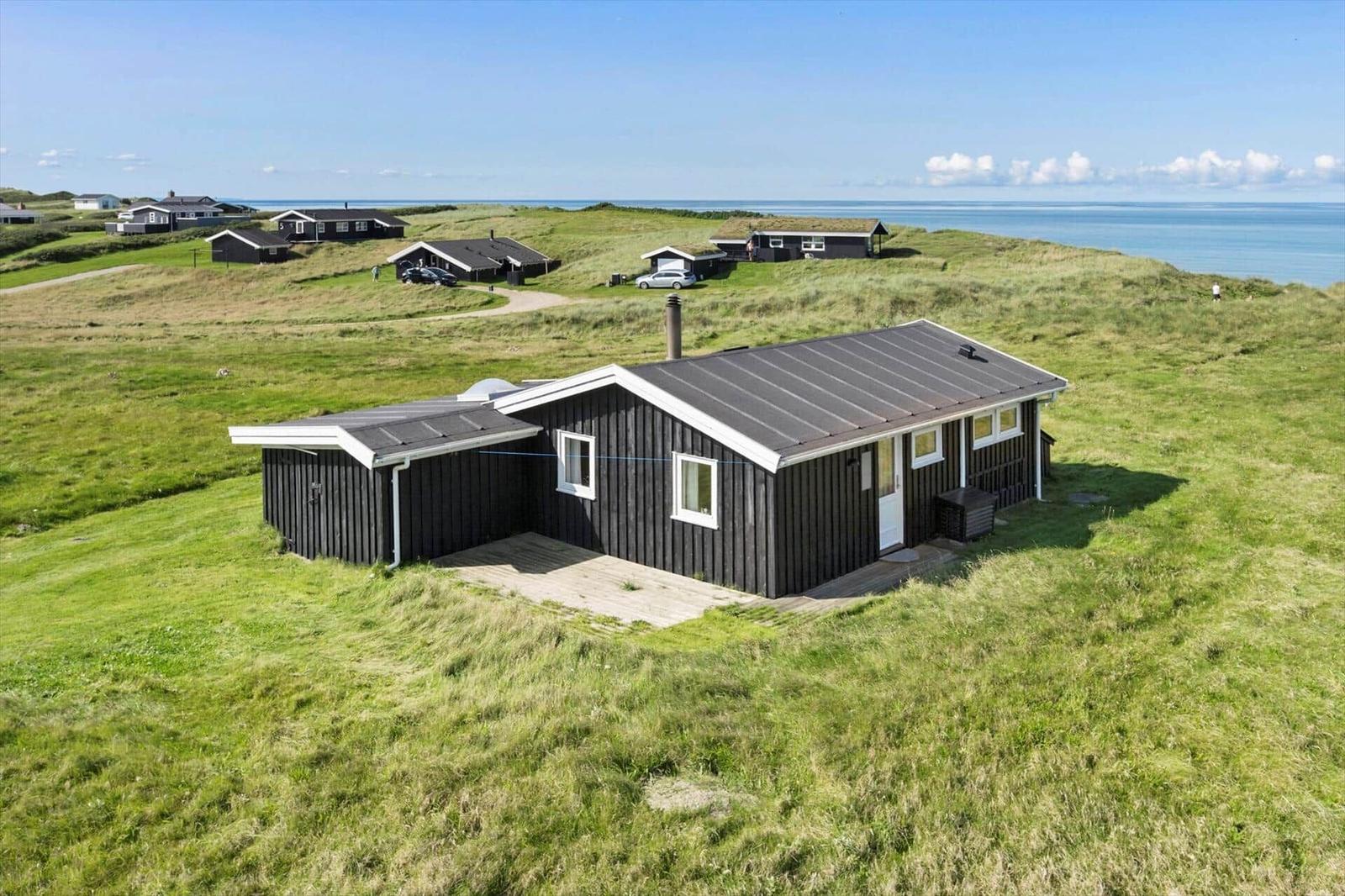 Schwarzes Holzhaus auf grüner Wiese mit Blick aufs Meer