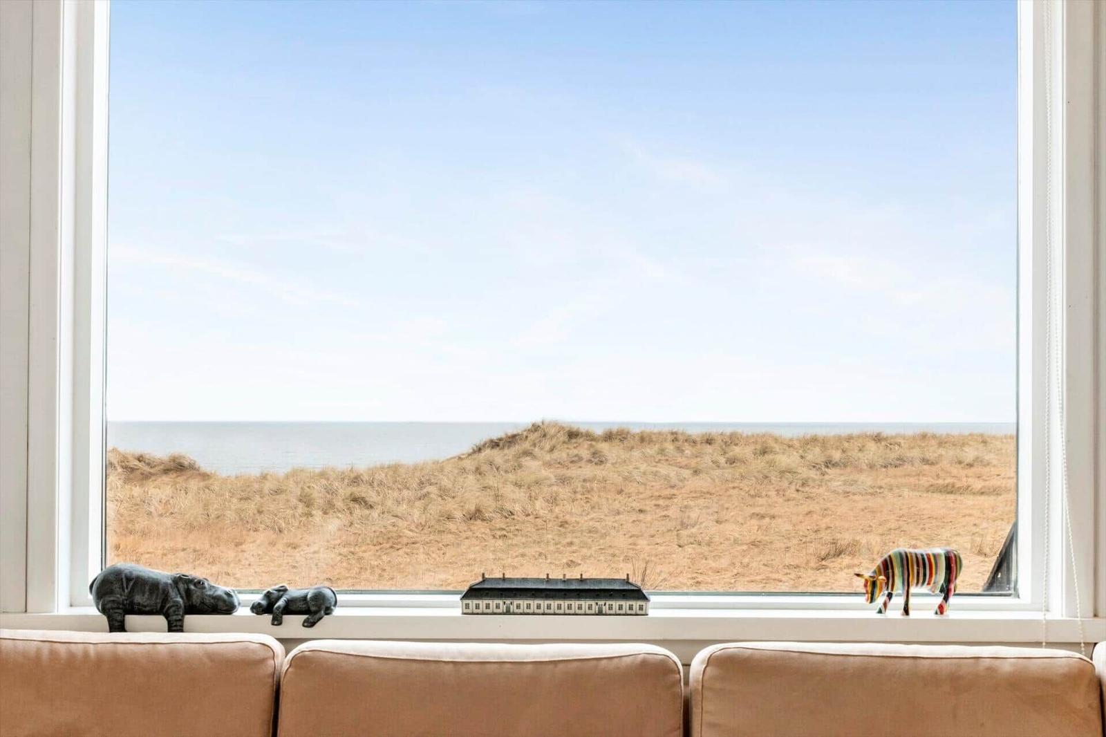 Von einem Fenster blickt man auf Dünen und Meer. Auf dem Fensterbrett stehen Figuren.
