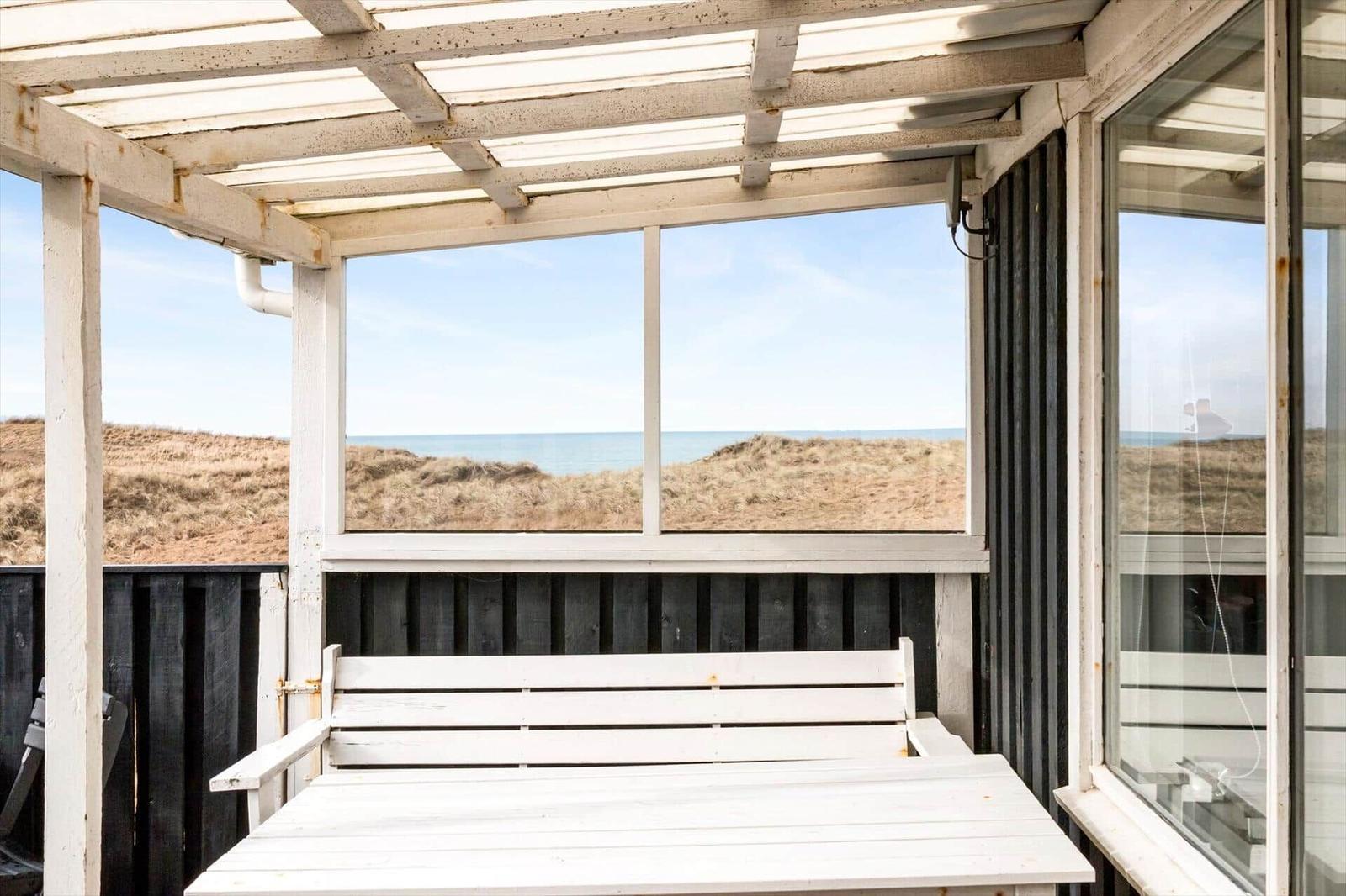 Terrasse mit weißem Tisch und Bank, Blick auf Strand und Meer.