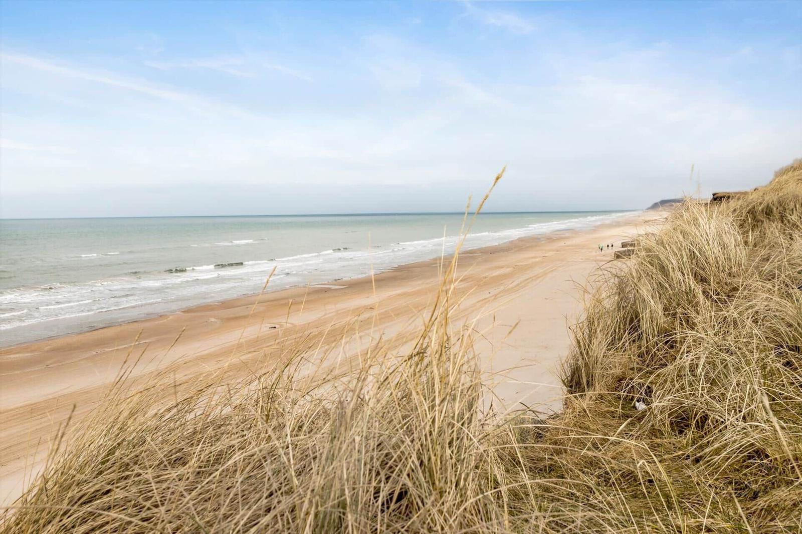 Strand mit Dünen und sanften Wellen im Hintergrund.
