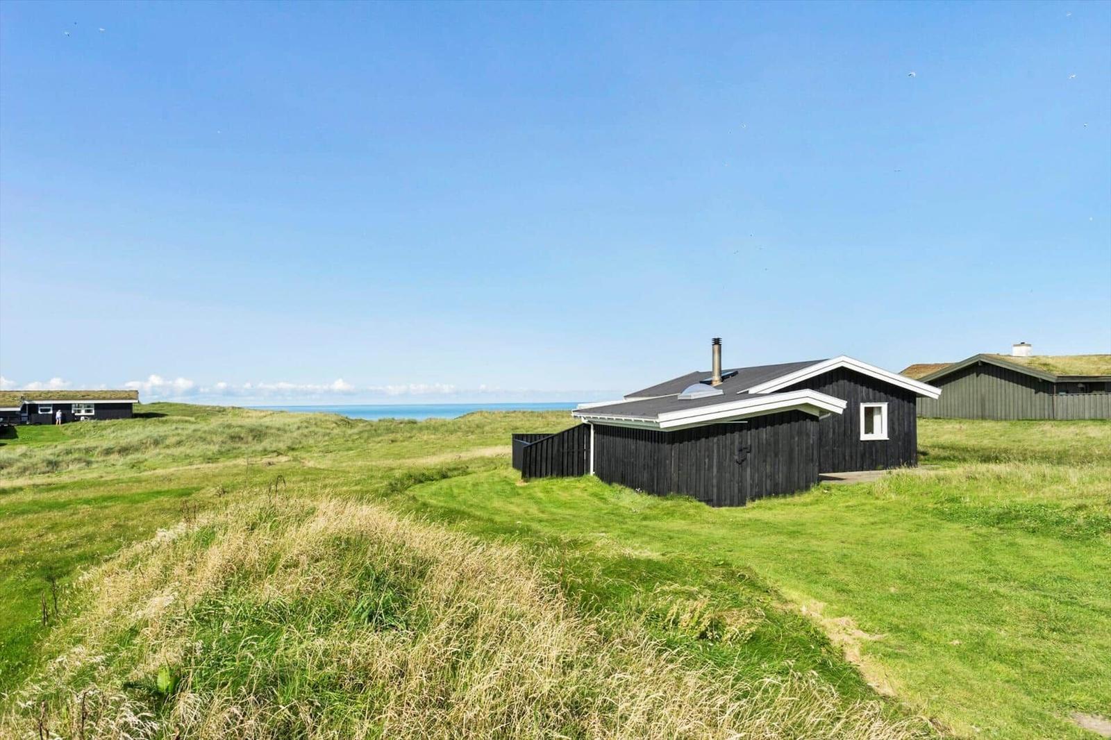 Schwarze Holzhütte auf grünem Hügelland mit Blick auf das Meer.