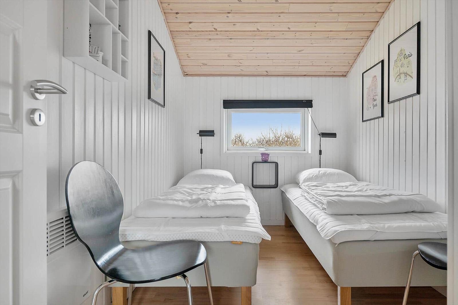 Two single beds, window with view, wooden ceiling and wall shelves.