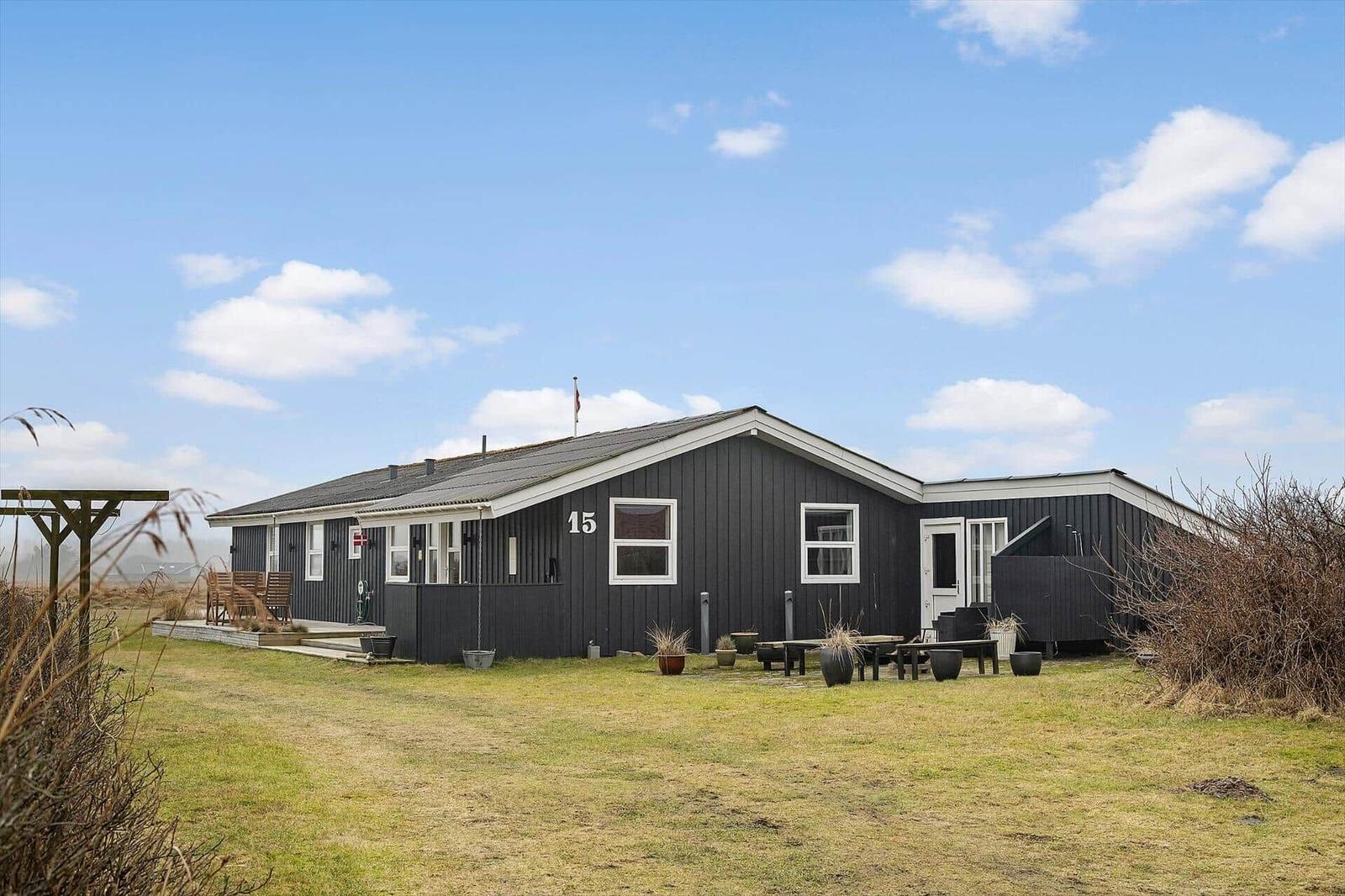 Black house with white trim and outdoor terrace under blue sky.