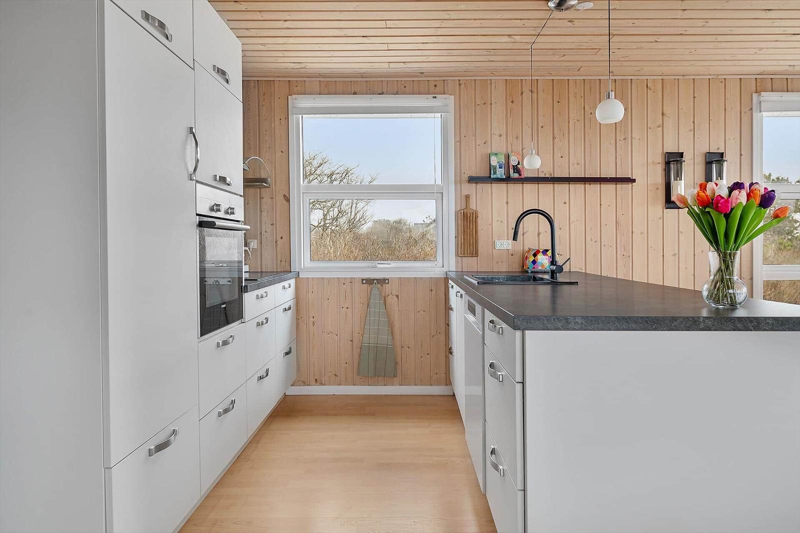 Kitchen with white cabinets, dark countertop, and wooden walls. Window with outdoor view.