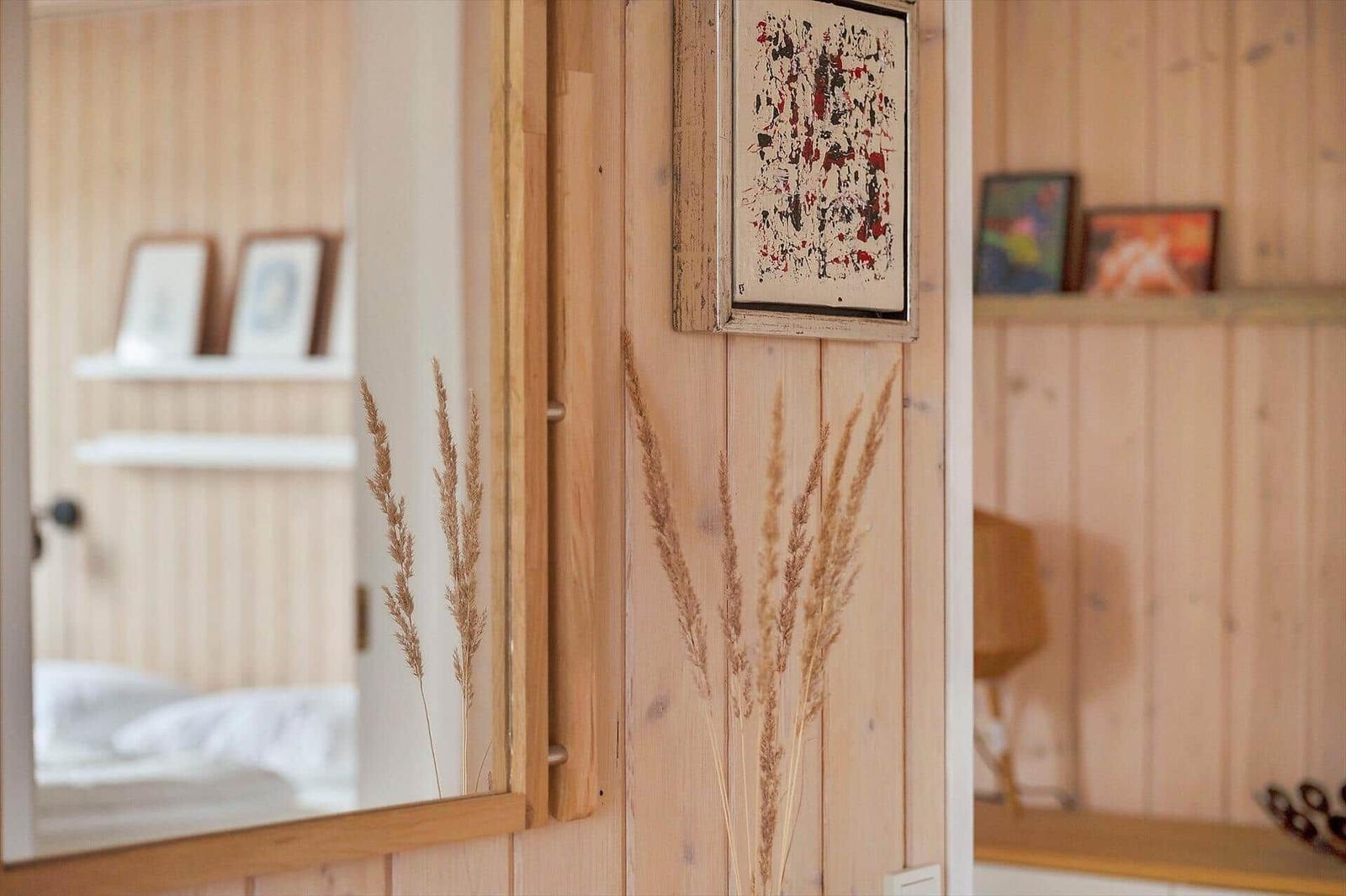 Mirror shows bedroom with wooden wall and pictures. Dried grass decorates the room.