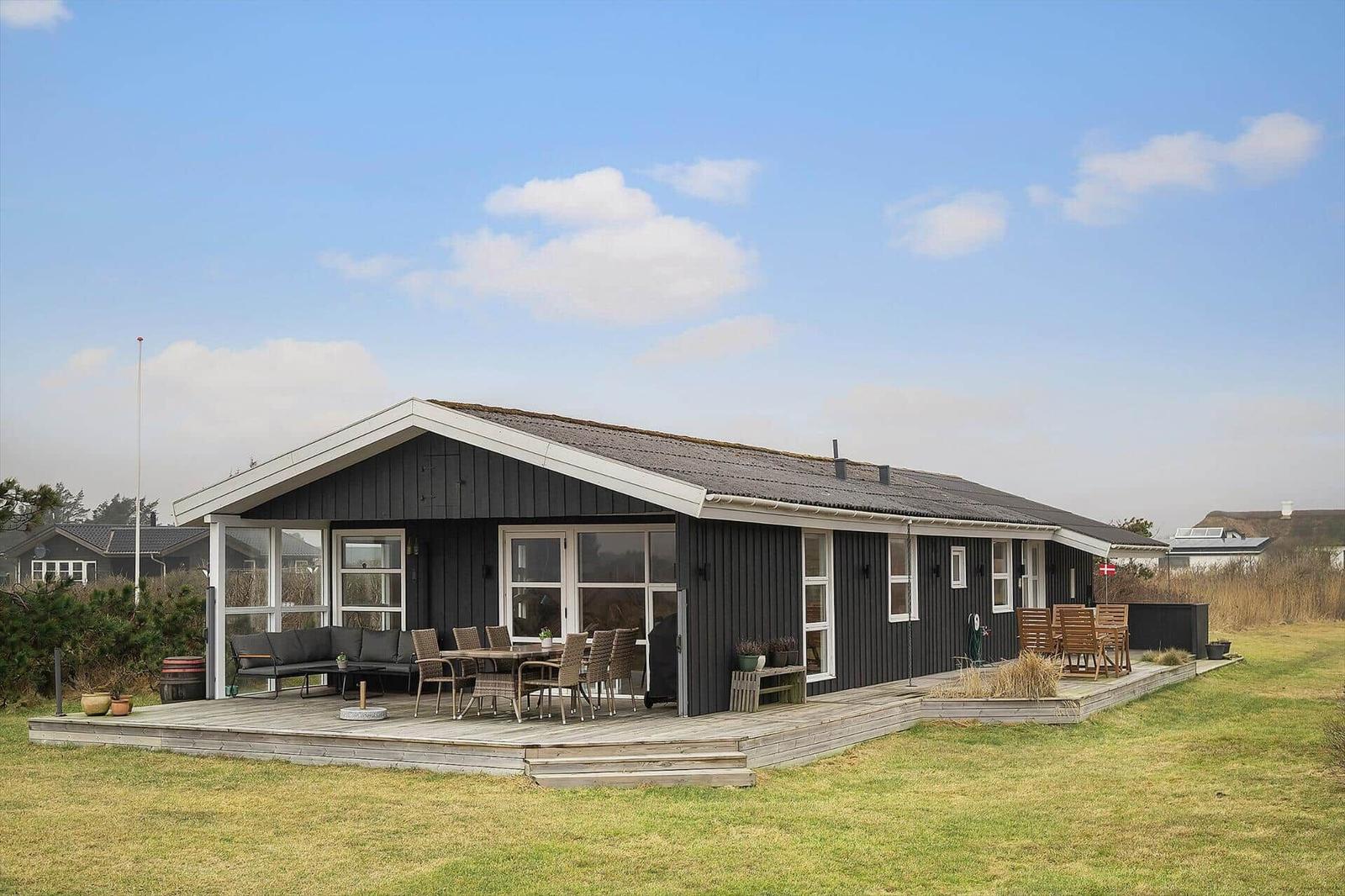 A house with dark cladding and wooden terrace. Outdoor seating is available.