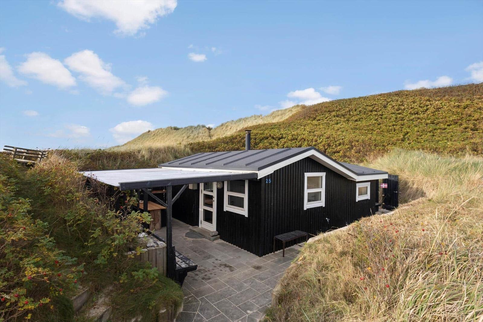 Schwarzes Ferienhaus mit Terrasse zwischen Dünen und Gras