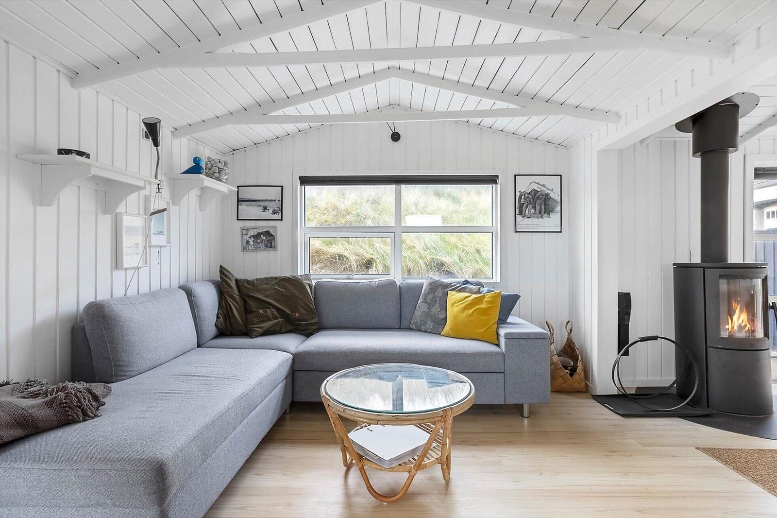 Ein Wohnzimmer mit grauem Sofa, runden Tisch und Kaminofen. Holzfußboden und weiße Wände.