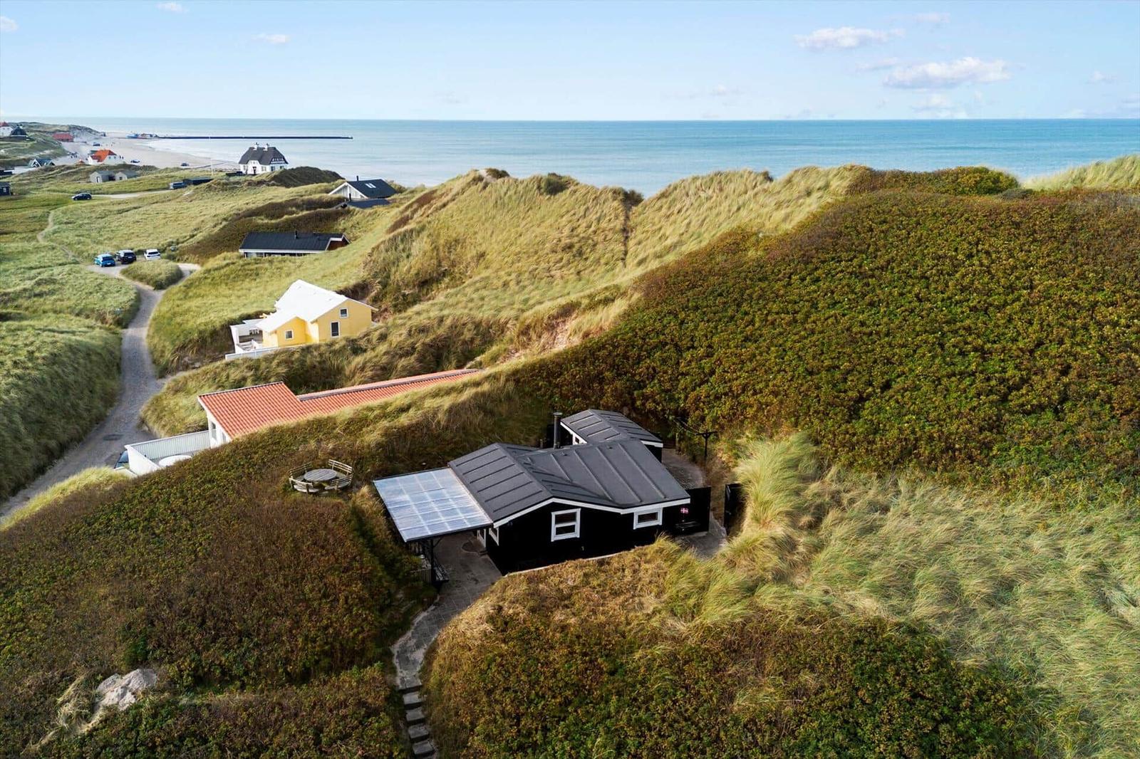 Schwarzes Haus mit Solaranlage auf Dünen, Blick auf Strand und Meer.