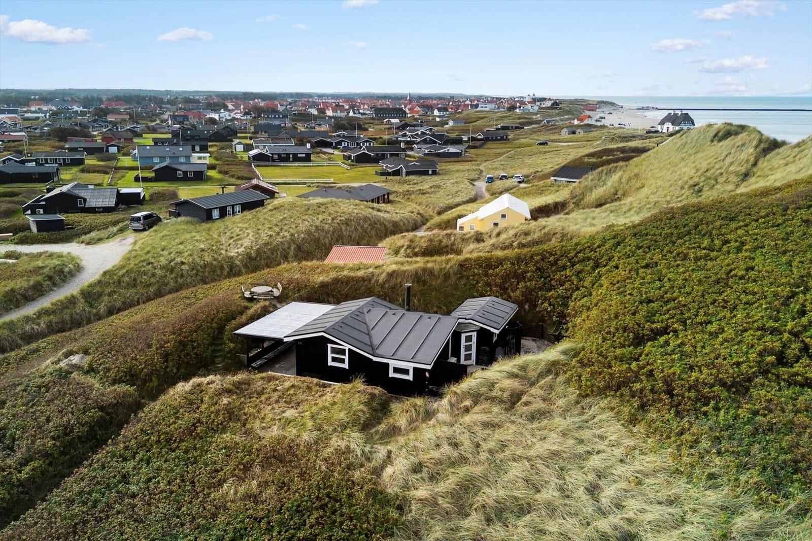 Schwarze Holzhütte auf Dünen mit Blick auf Küstenstadt und Strand.