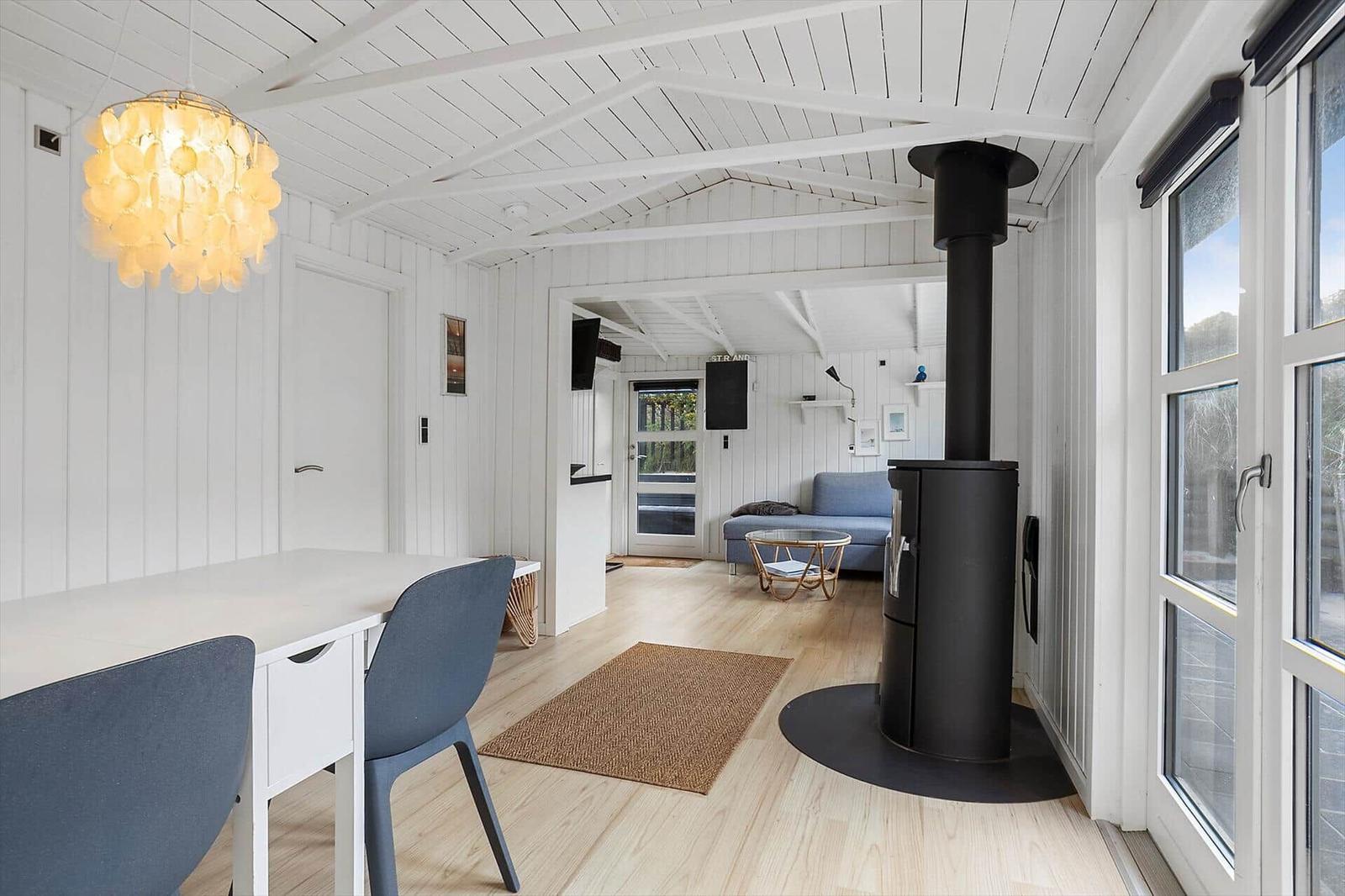 Wohnraum mit Esstisch, Kamin und Sofa. Weiße Wände, Holzboden und große Fenster.