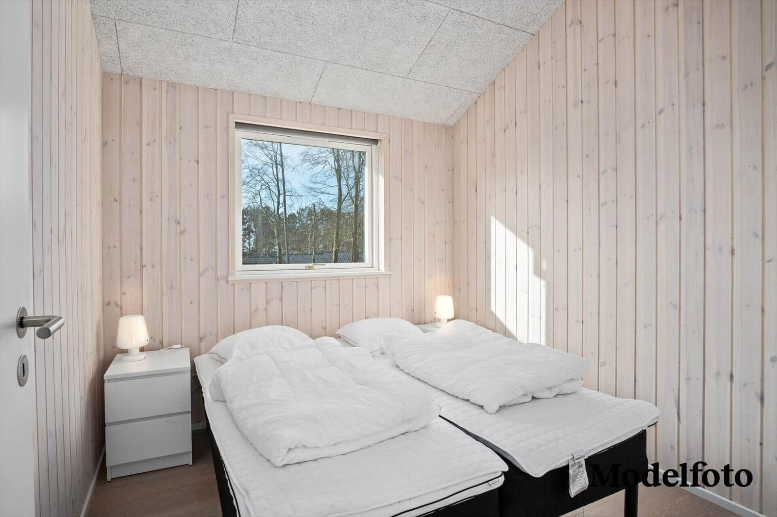 Bedroom with two beds, wooden walls, and window with view of trees.