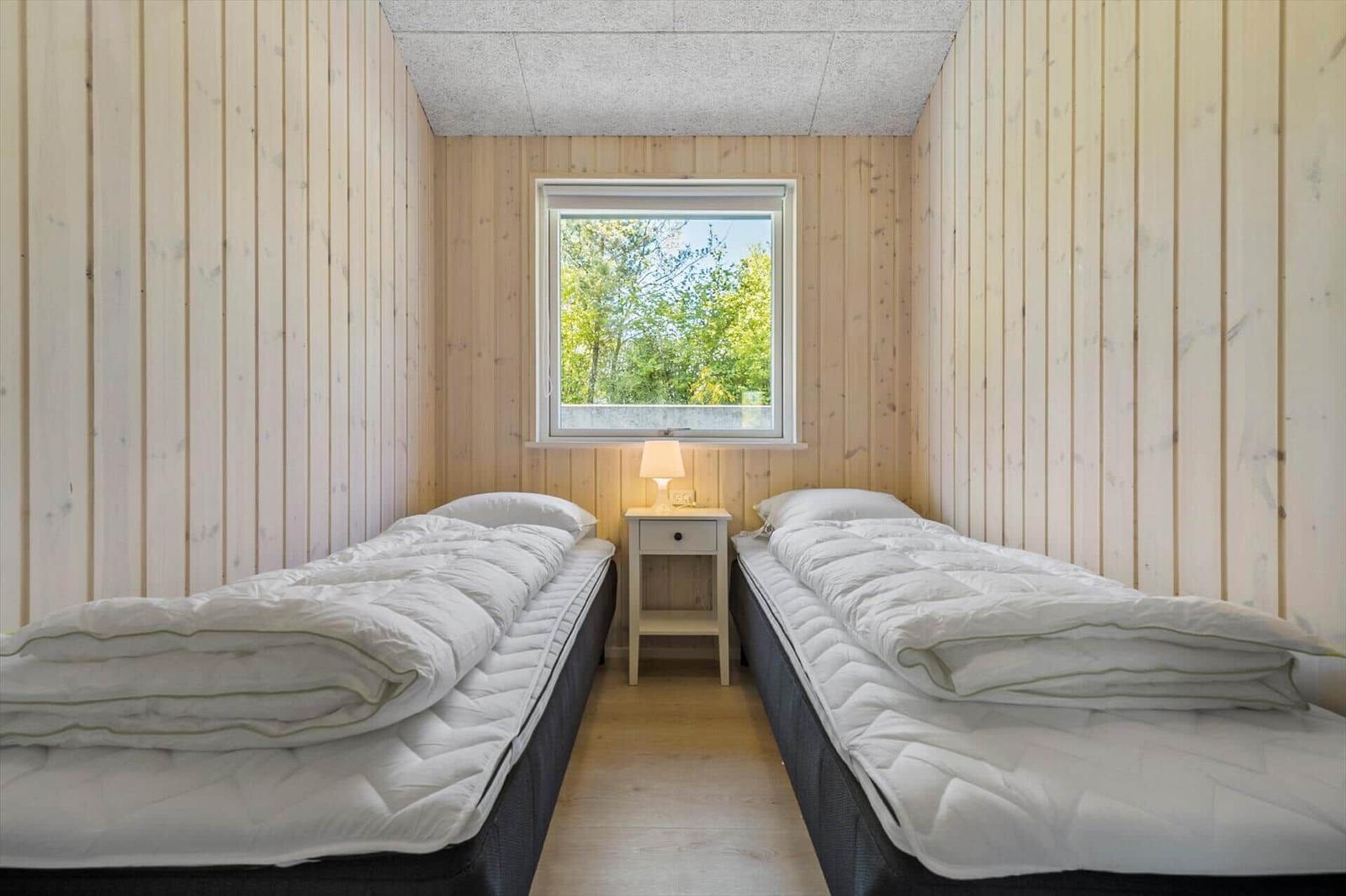 Two beds with white covers are in a room with wooden walls and a window.