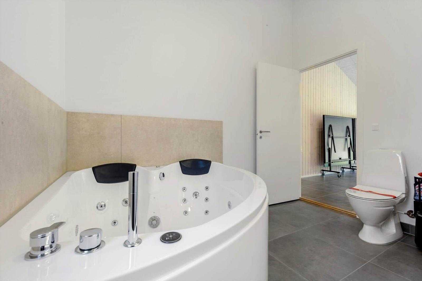 Bathroom with whirlpool tub, toilet, and door to adjacent room.
