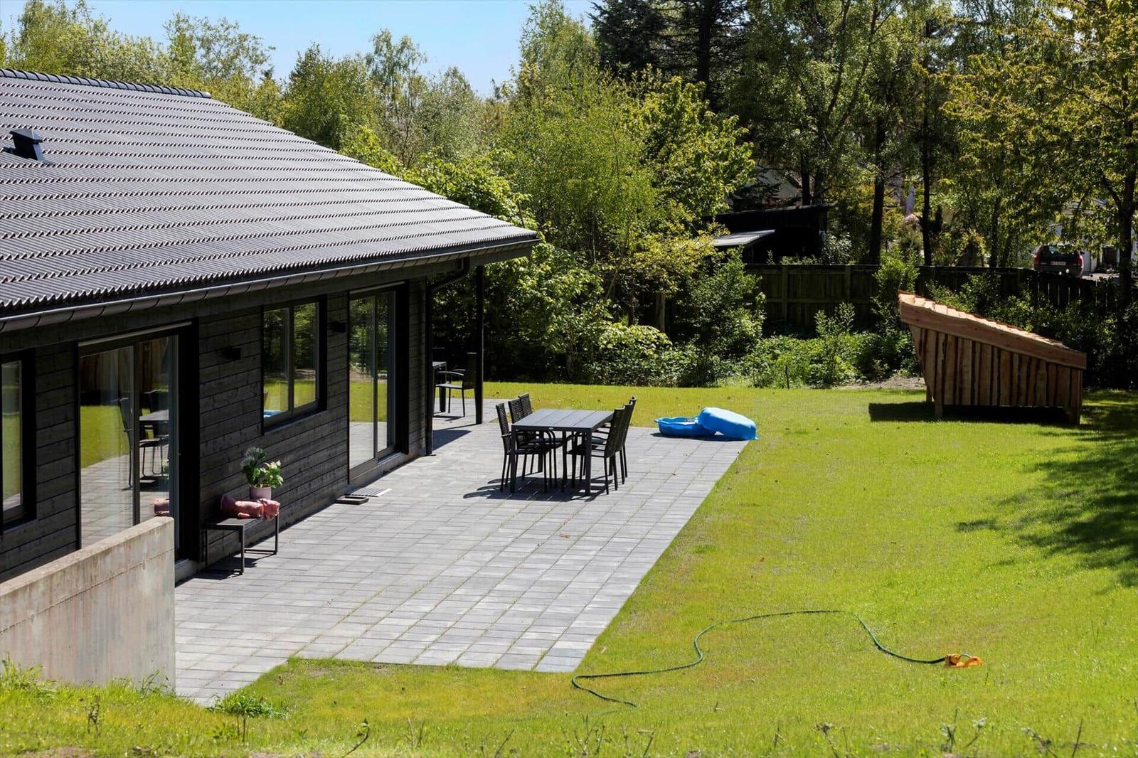 House with terrace, garden, and wooden shed. Table and chairs are outside.