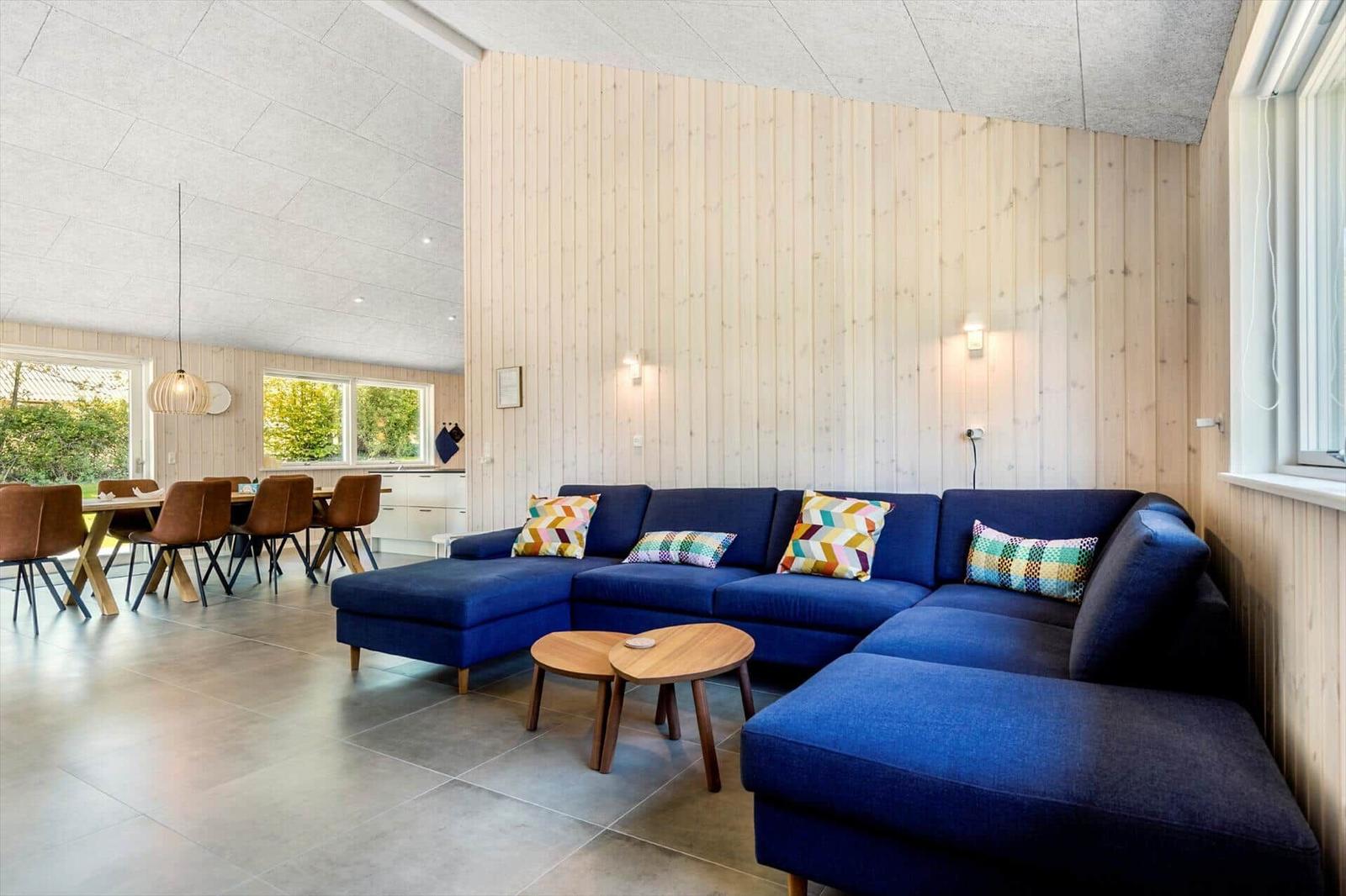 Living room with blue sofa and wooden wall. Dining area with table and chairs in background.