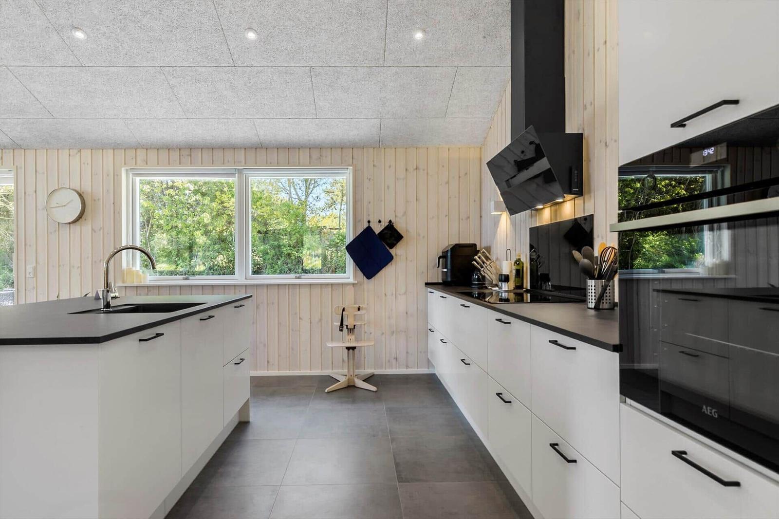 Modern kitchen with white countertop and wooden wall. Window with view of greenery.