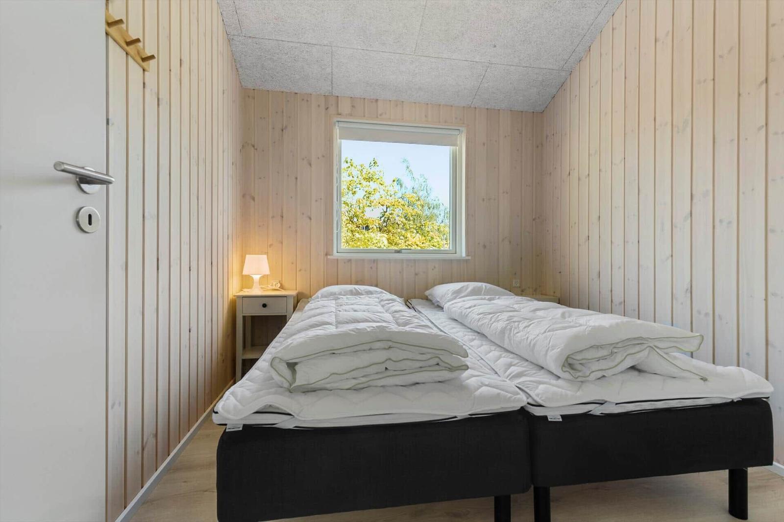 Room with two beds, wooden walls, and window with view of trees.