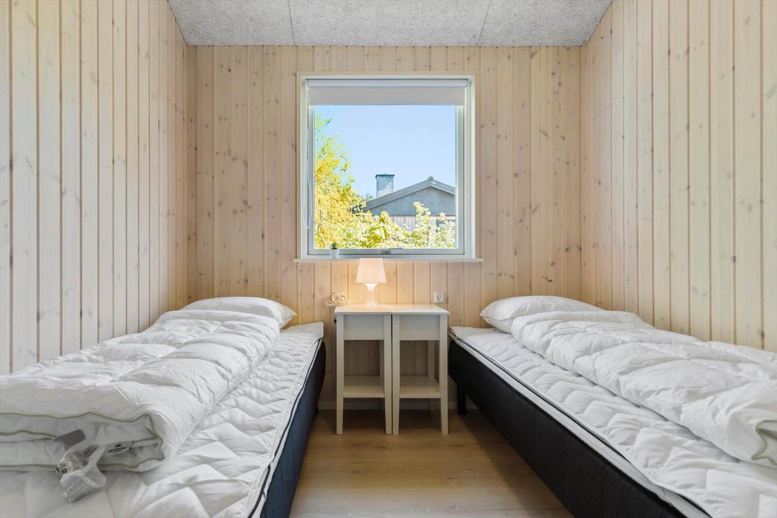 Two beds with white bedding are in a wooden room with a window.