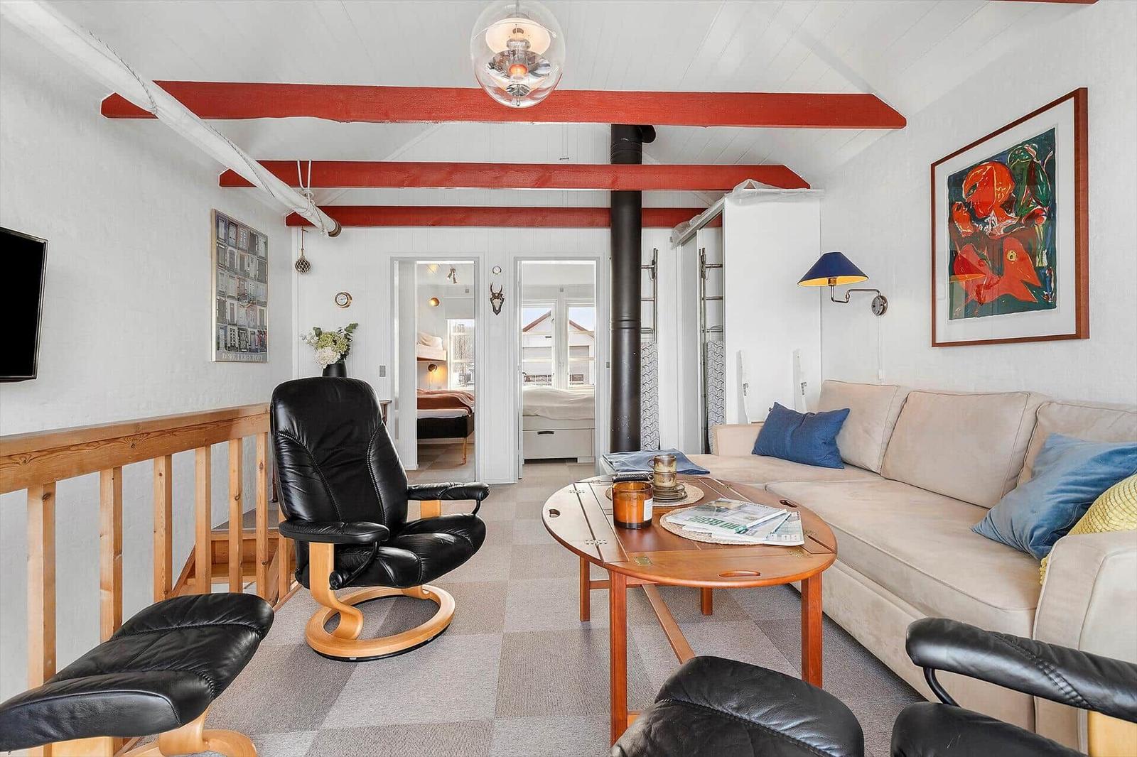 Living room with sofa, black chairs, and wooden table. Red beams on ceiling.