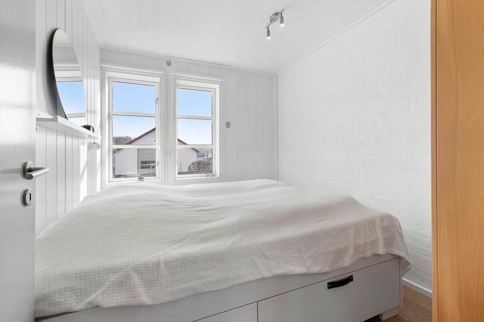 Bedroom with bed, windows, and mirror on the wall.