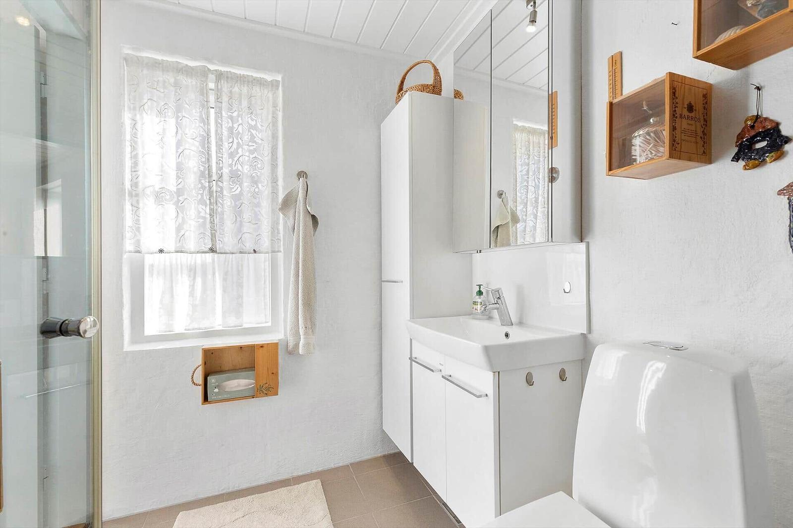 Bathroom with shower, sink, and toilet. Window with curtain and wooden shelves.