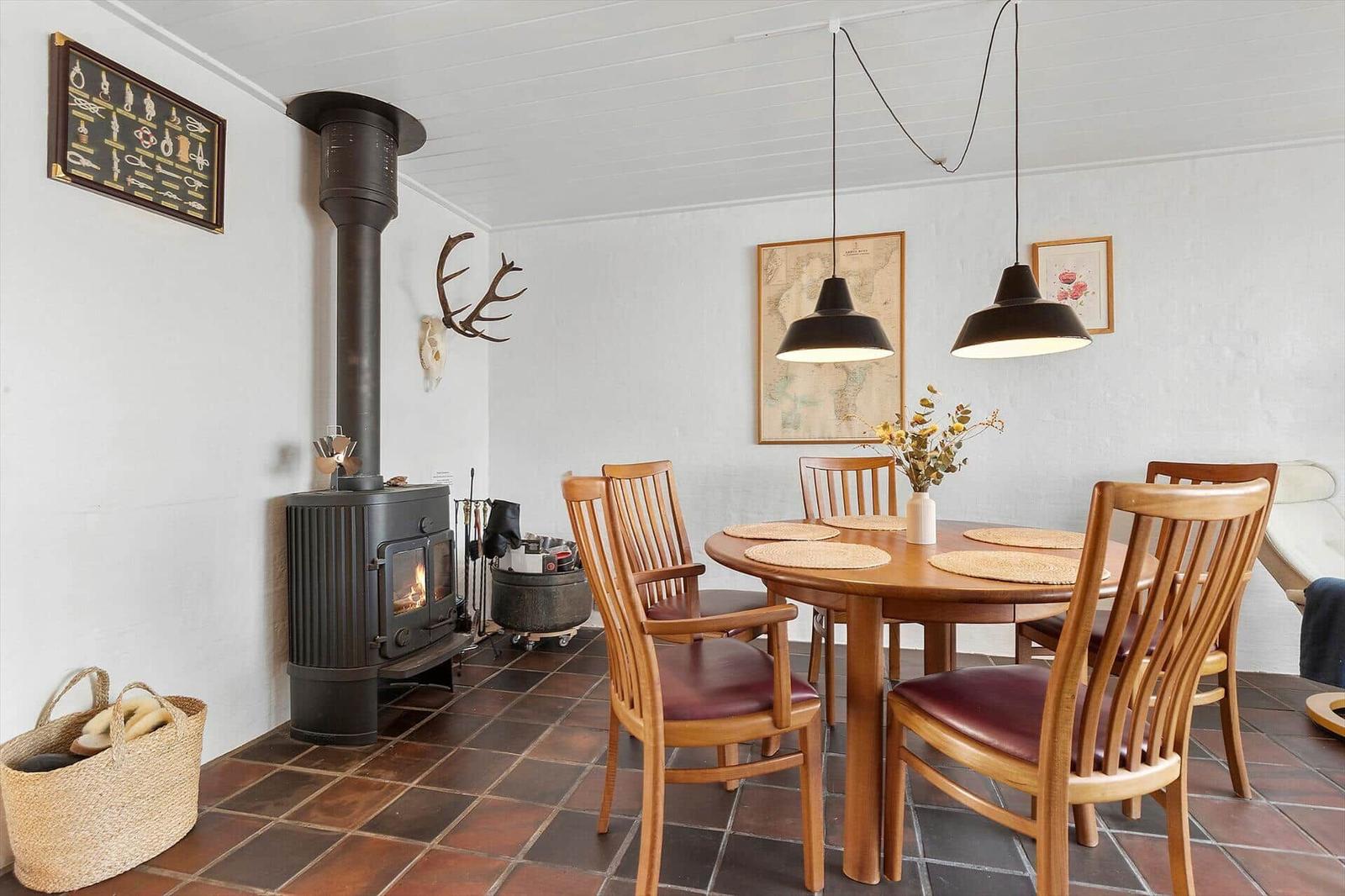 Dining room with wooden table, chairs, and wood stove. Wall decor and pendant lights.