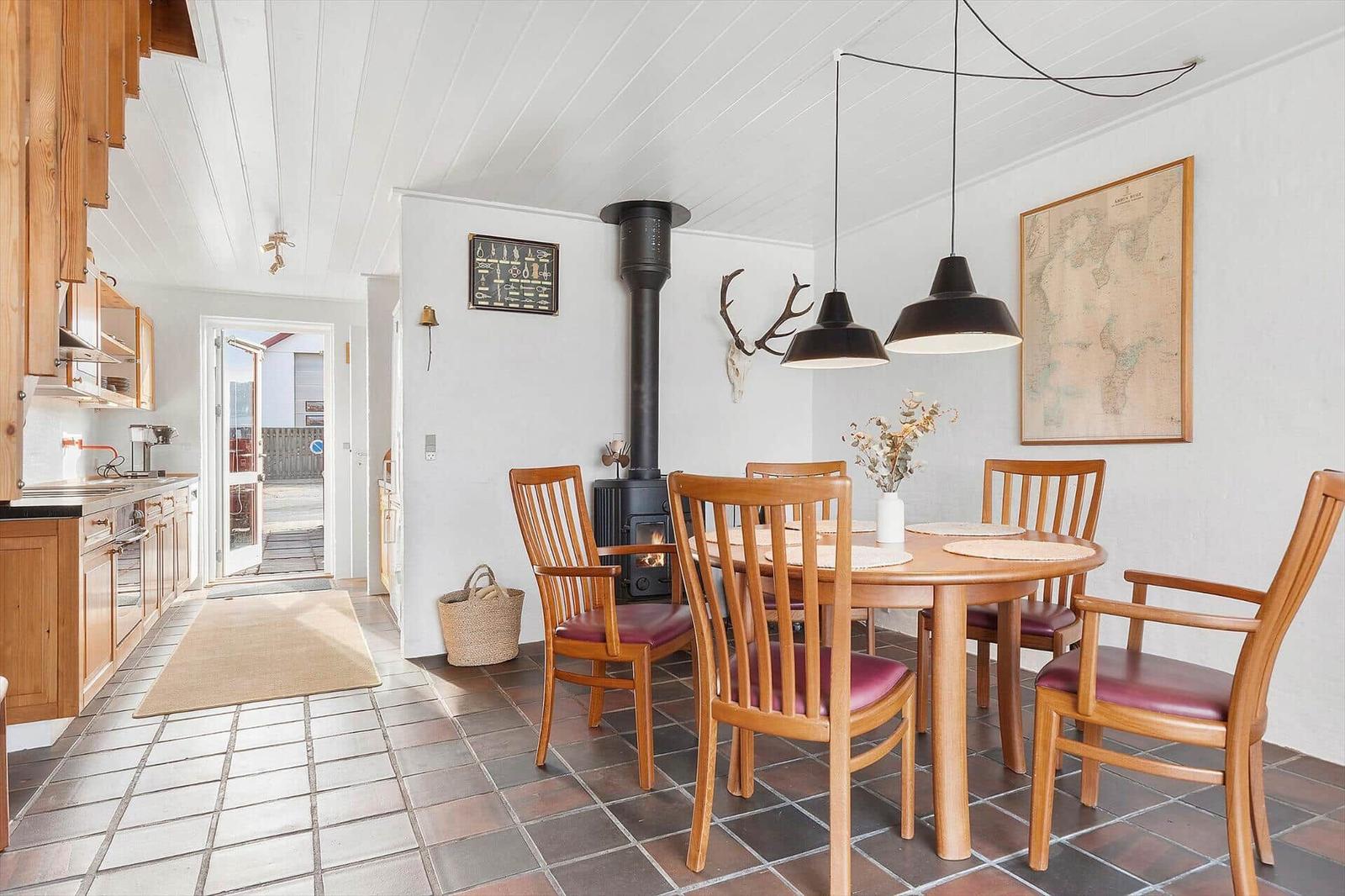 Dining room with wooden table, chairs, and wood stove. Kitchen on left. Wall map and deer antlers.
