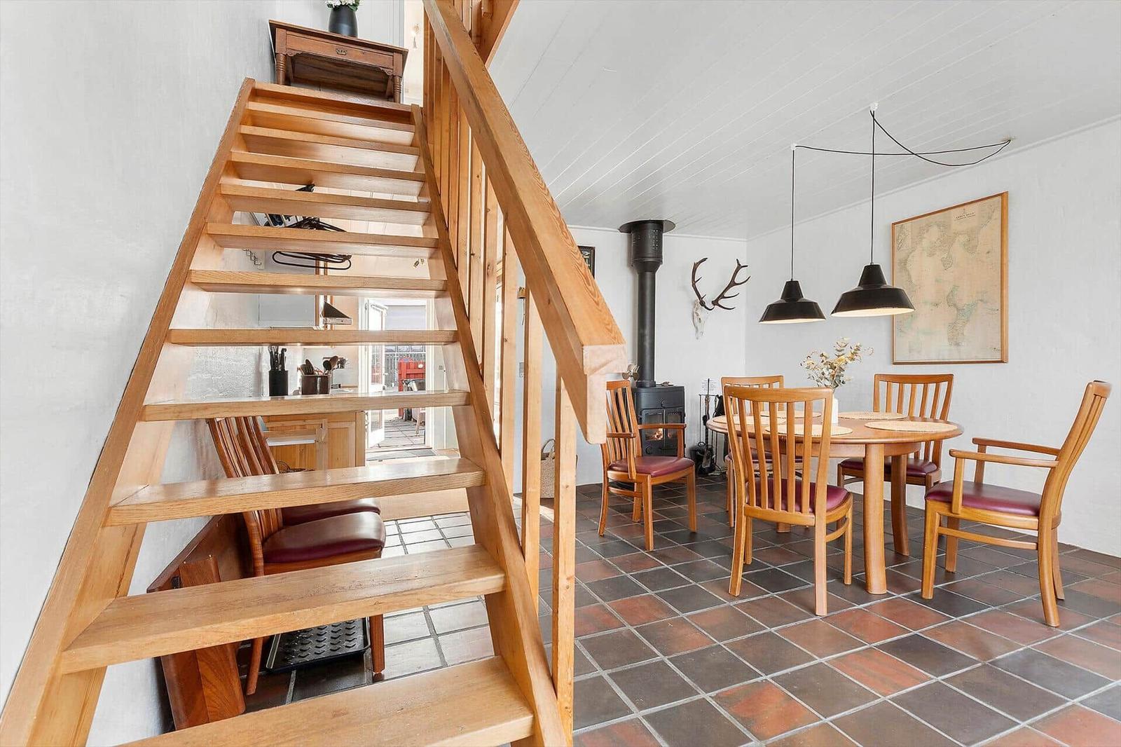 Wooden staircase leads to kitchen. Dining area with table, chairs, and stove.