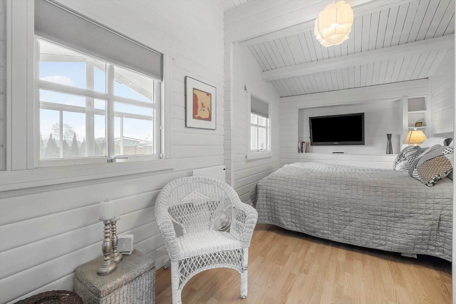 Schlafzimmer mit Bett, Fernseher und weißem Stuhl. Holzfußboden und Fenster mit Blick.