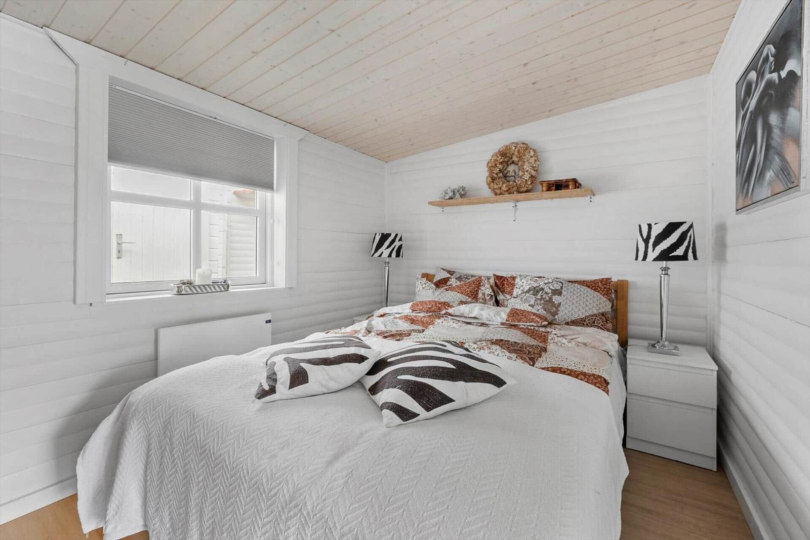 Schlafzimmer mit Bett, Nachttischen und Fenster. Wände und Decke sind weiß verkleidet.
