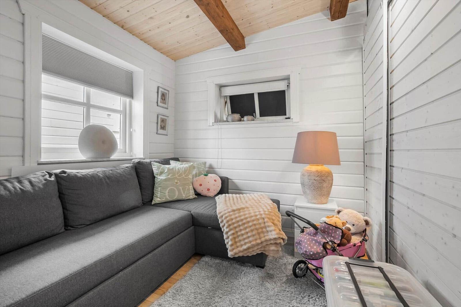 Ein Wohnzimmer mit grauem Sofa, weißen Wänden und Holzbalken an der Decke.