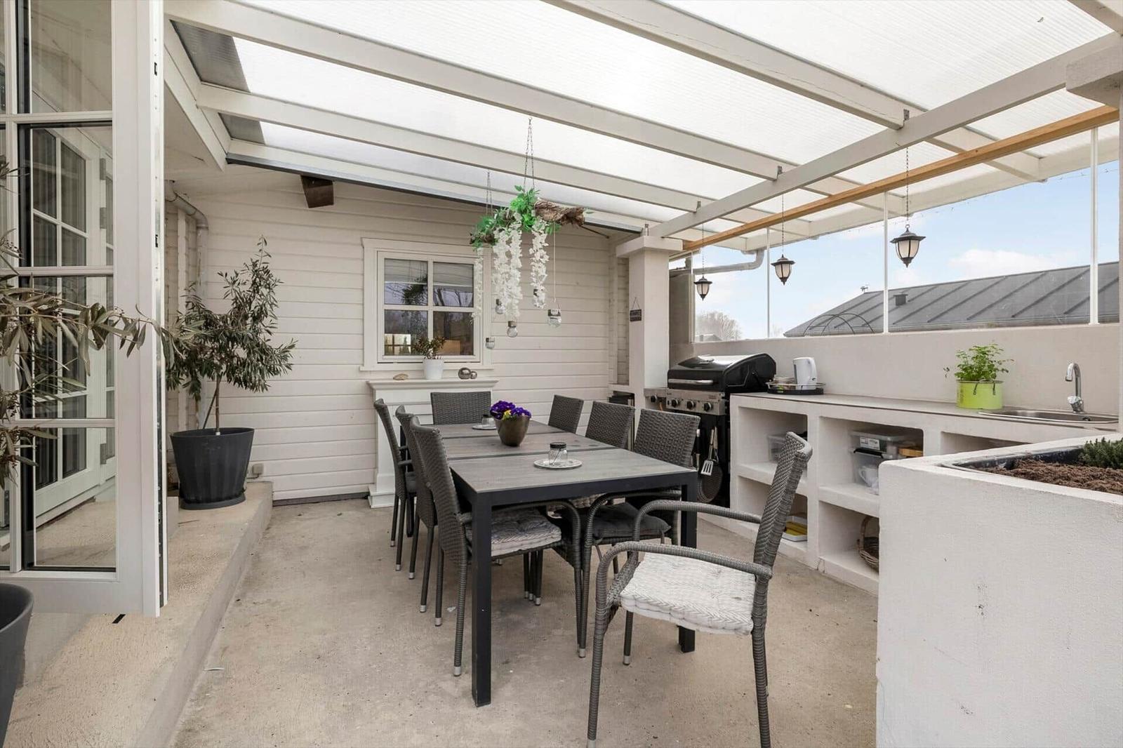 Terrasse mit Essbereich, Grill und Küchenzeile unter Dach.
