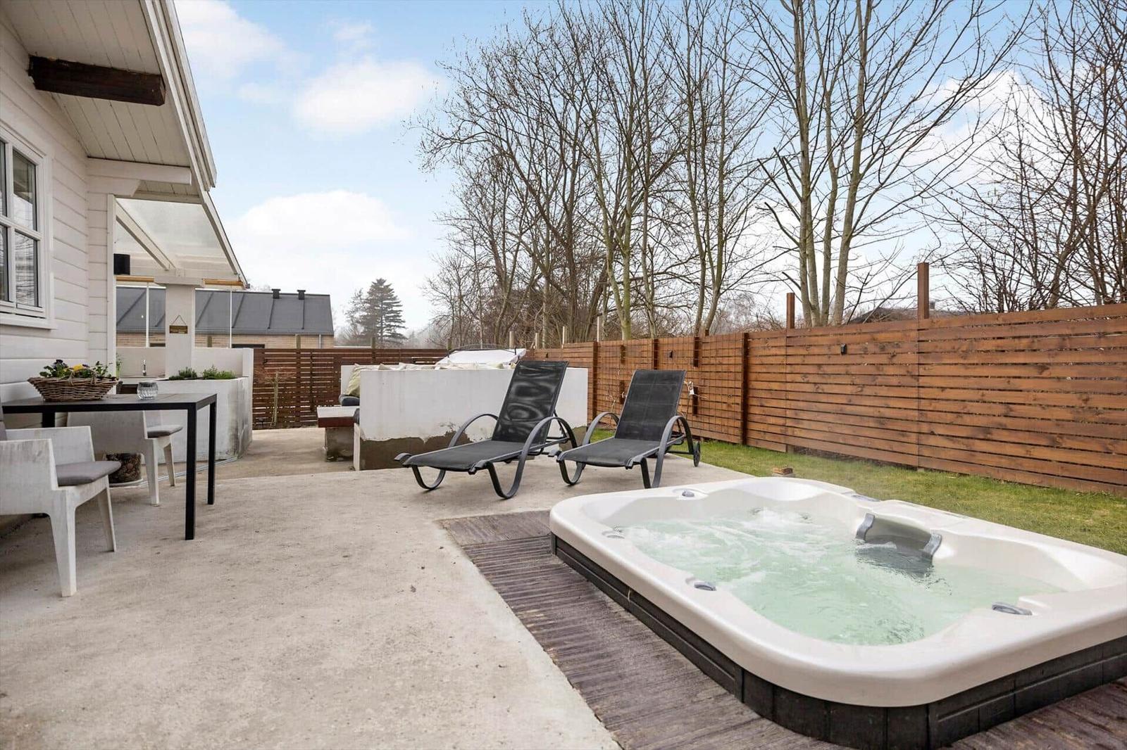 Außenbereich mit Whirlpool, Liegestühlen und Tisch. Hinterhof mit Holzzaun und Bäumen.
